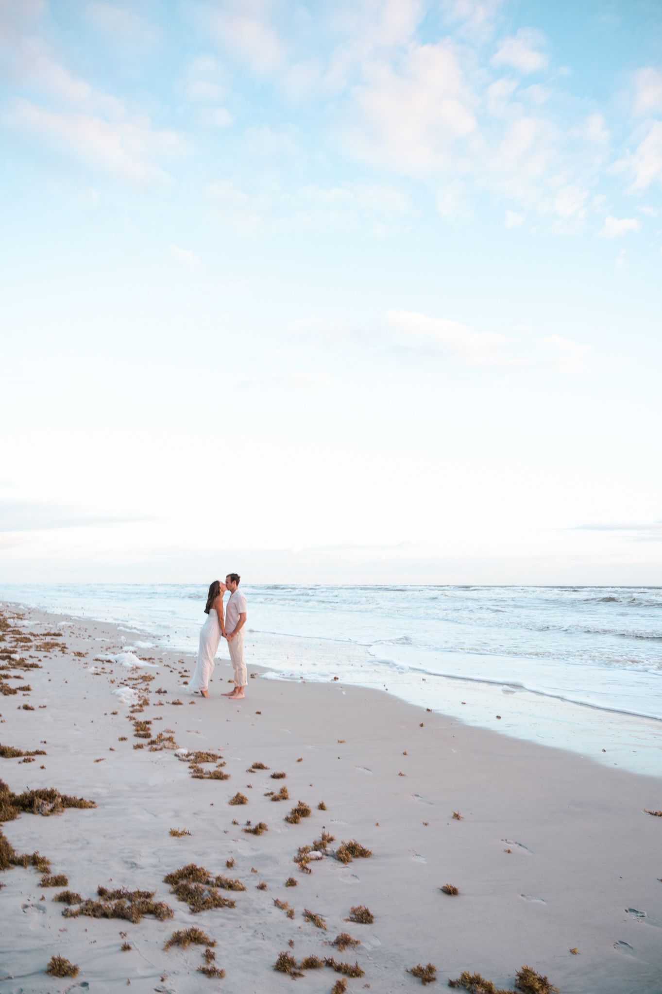 Romantic beach scene with couple walking along shoreline at sunset.