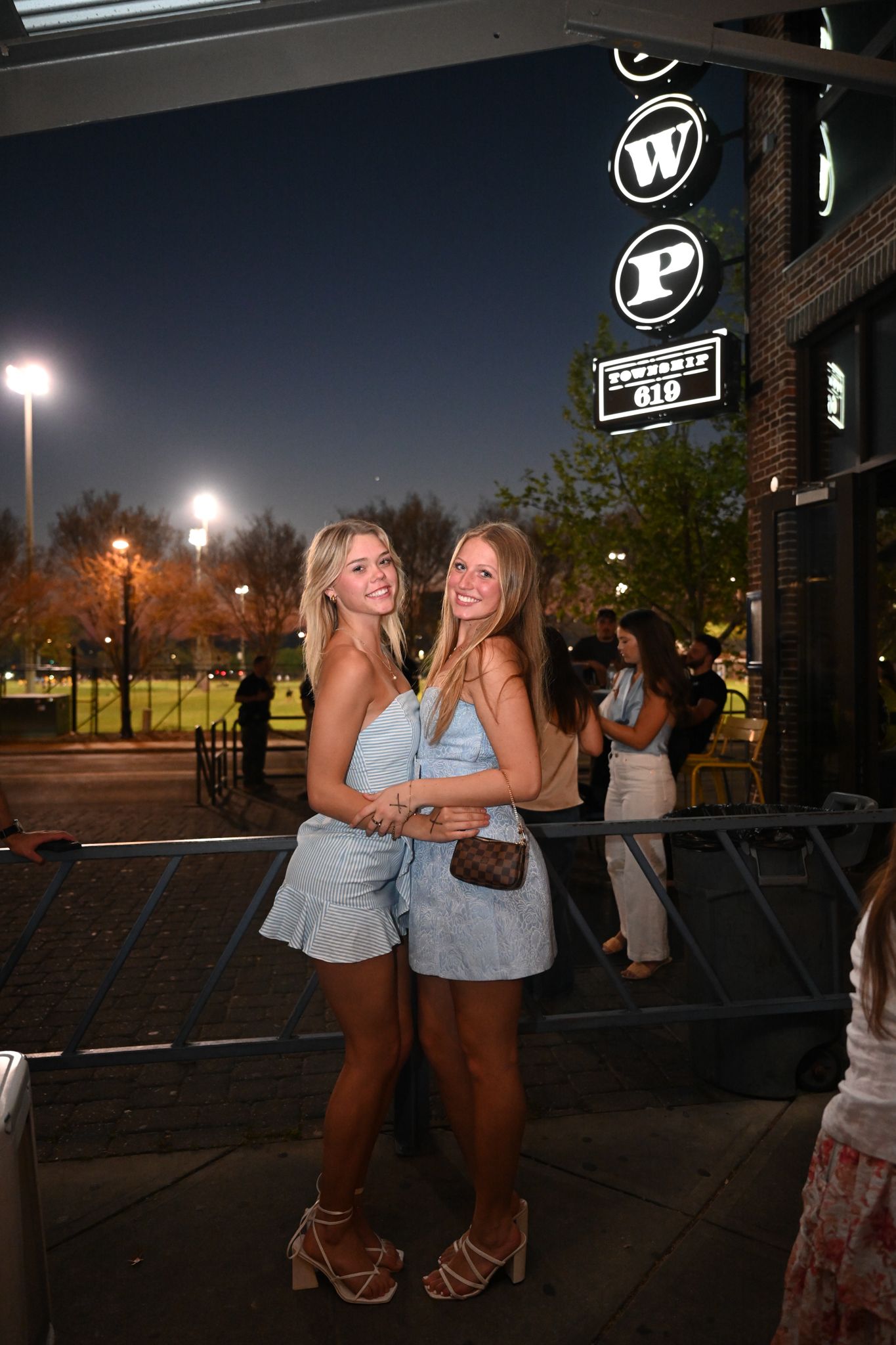 Two young women in matching blue outfits pose together smiling outside a venue at night.