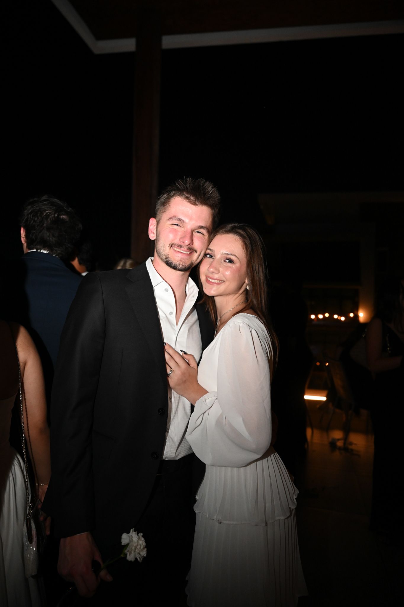 A smiling couple poses together at a formal evening event, man in black suit, woman in white dress.