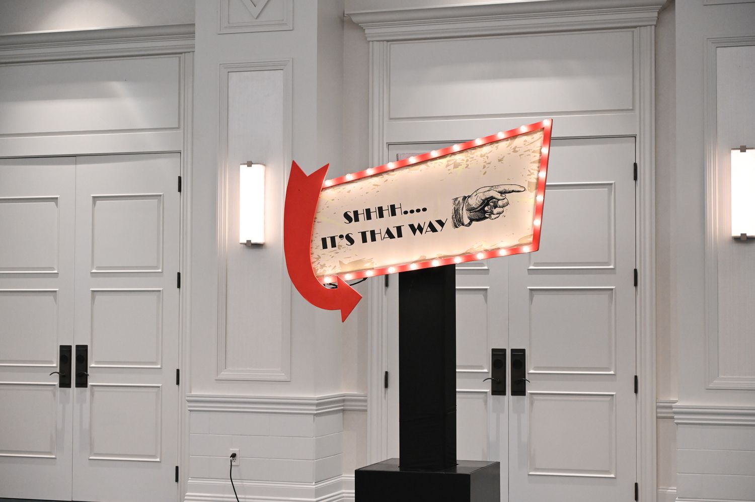 Vintage-style directional arrow sign on a black pedestal in an elegant white-paneled event venue.
