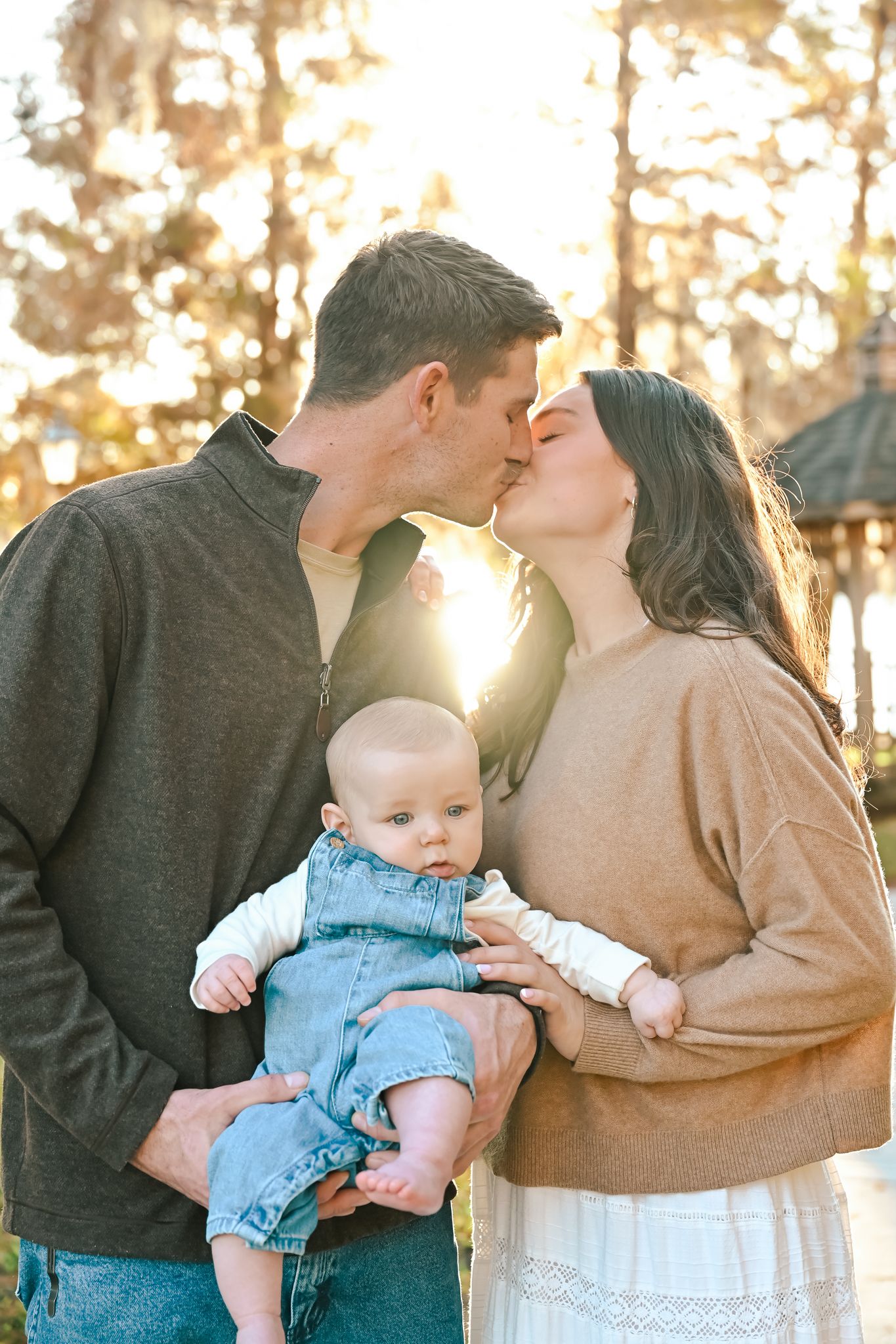 Romantic sunset photos of a couple with their baby in a park setting.