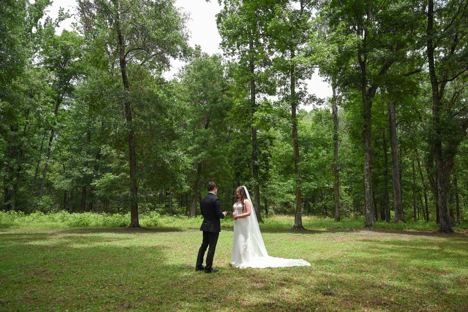 A bride and groom stand together in a lush green forest clearing during their outdoor wedding ceremony.