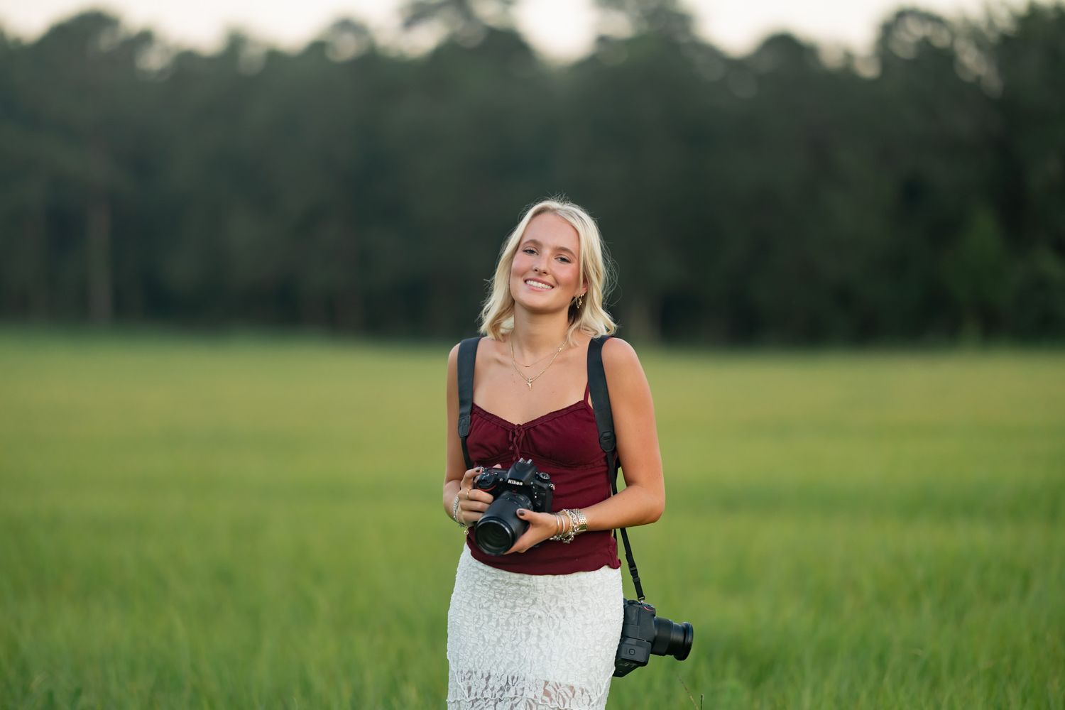 Professional photographer with camera standing in a lush green field at golden hour.