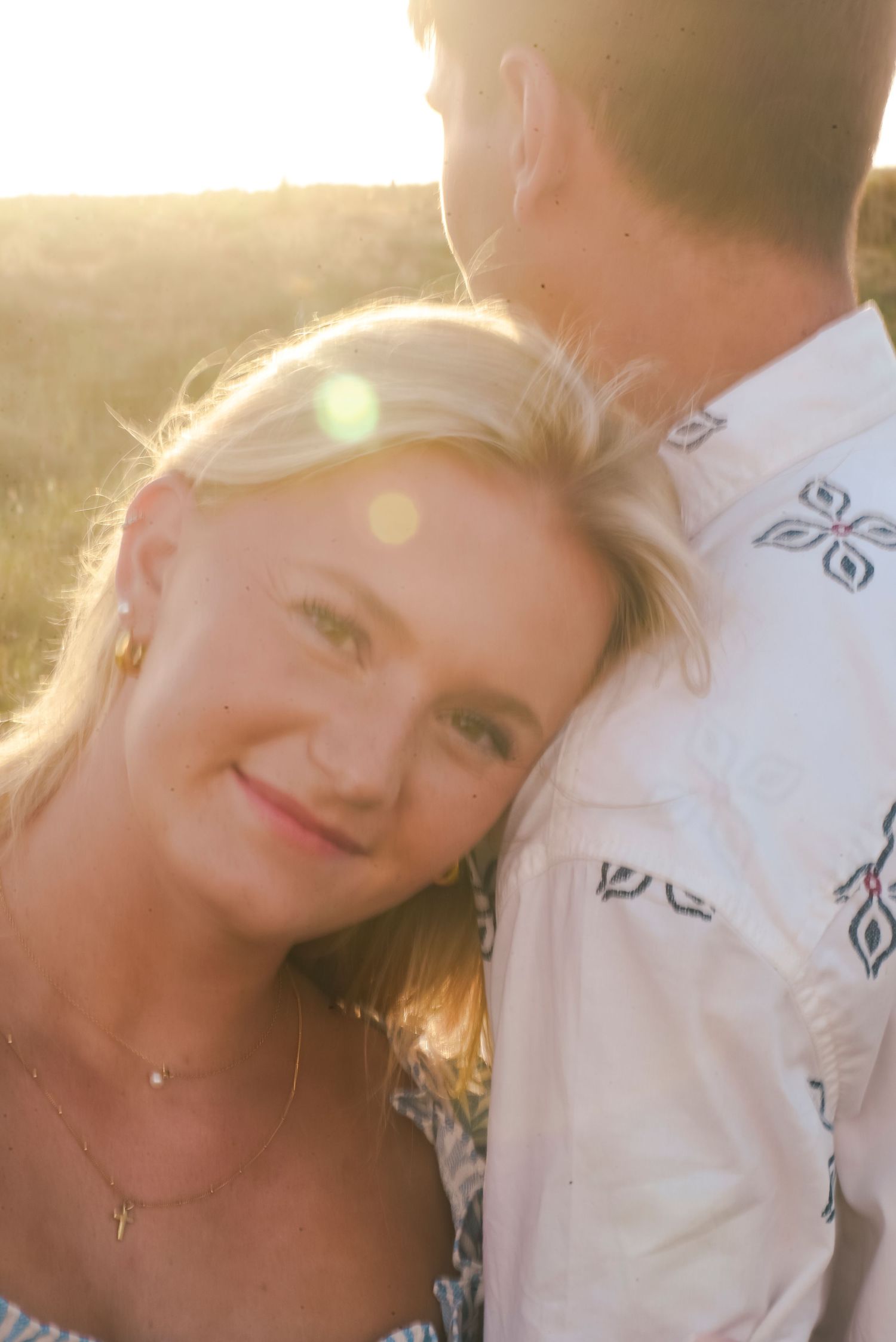 A young blonde woman rests her head on a man's shoulder during a golden hour outdoor photo session.