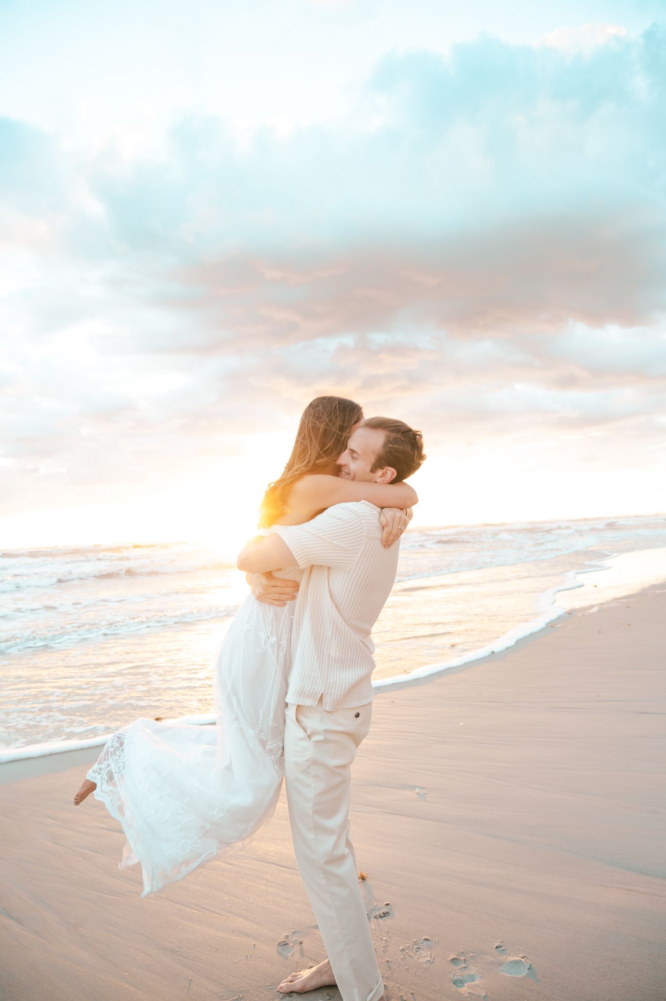 Romantic beach wedding photoshoot with couple embracing at sunset on sandy shore.