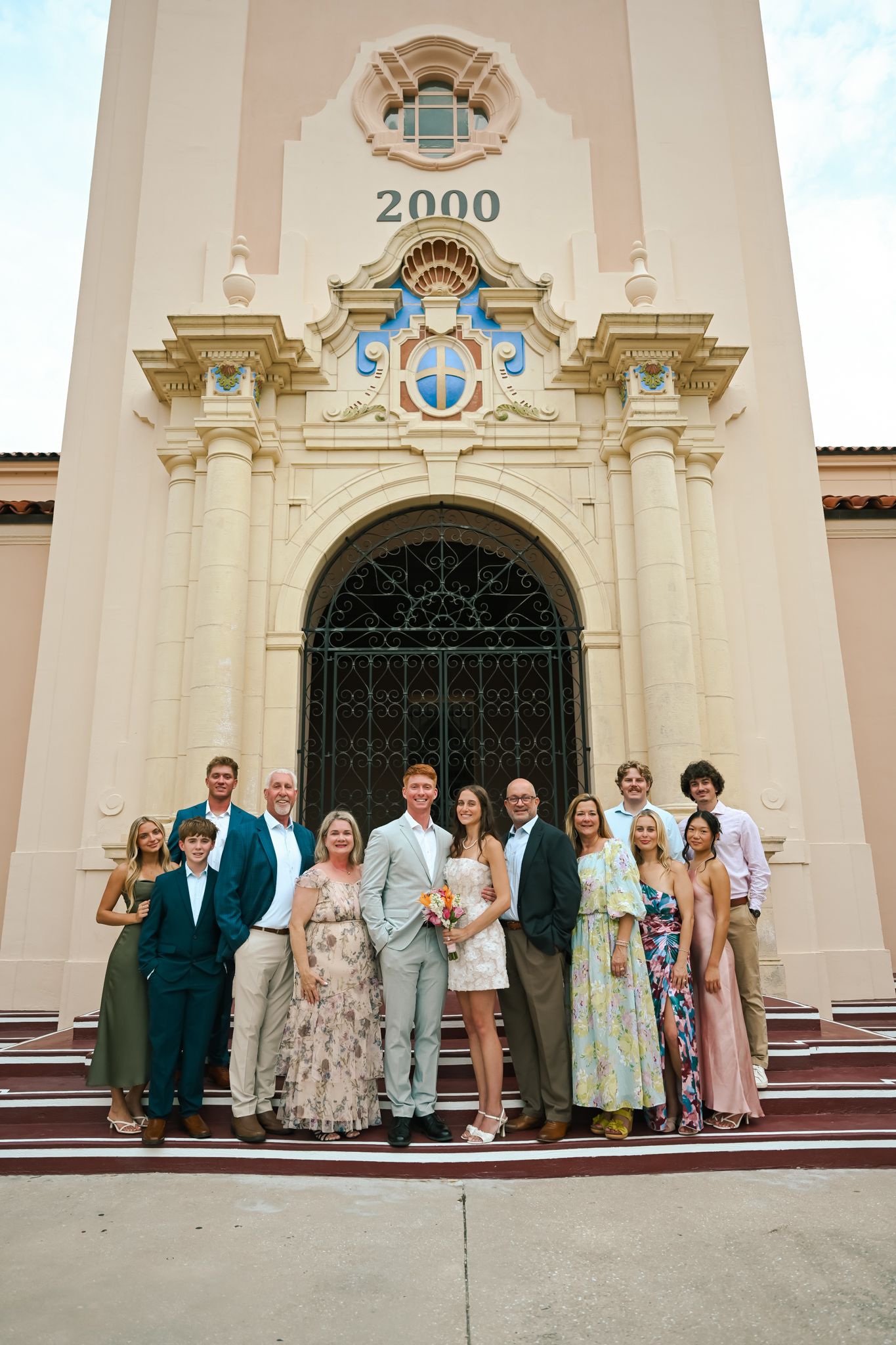 Family group photo on steps of elegant Spanish Colonial building with ornate facade and arched doorway.