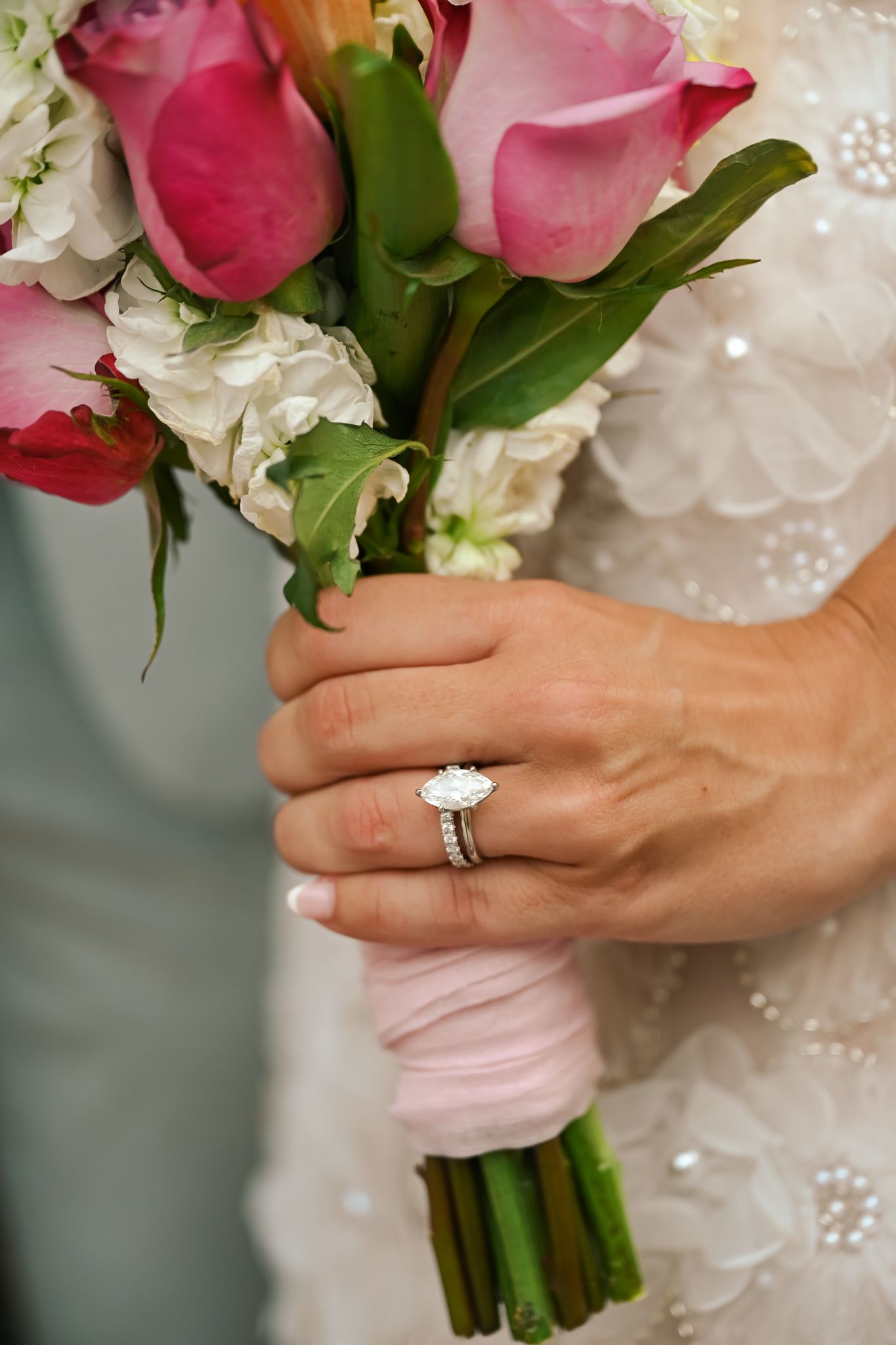 Bride holding pink rose wedding bouquet wrapped in ribbon, showcasing elegant diamond engagement ring on her finger.