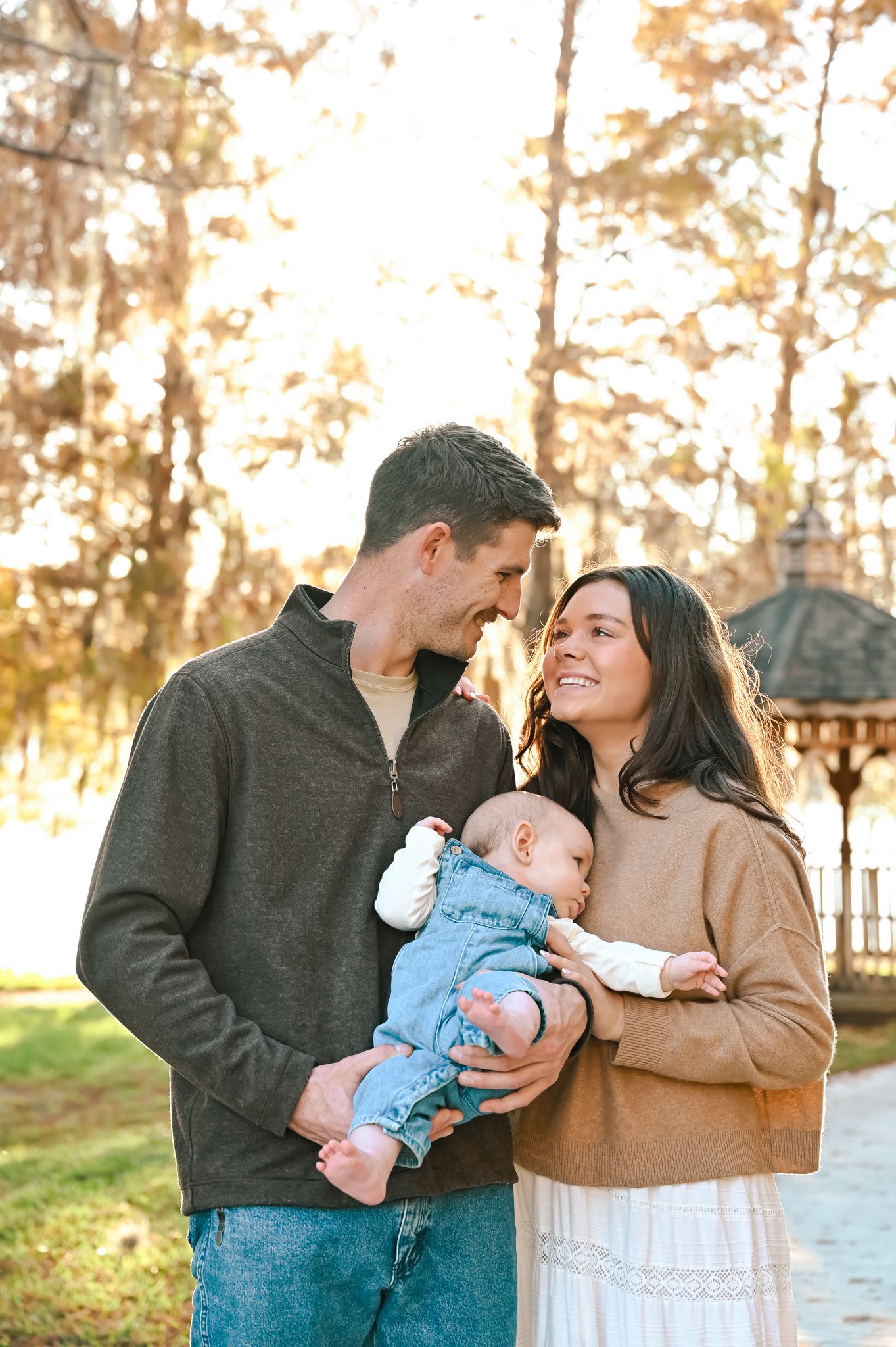 An intimate family portrait with a baby in denim overalls during sunset.