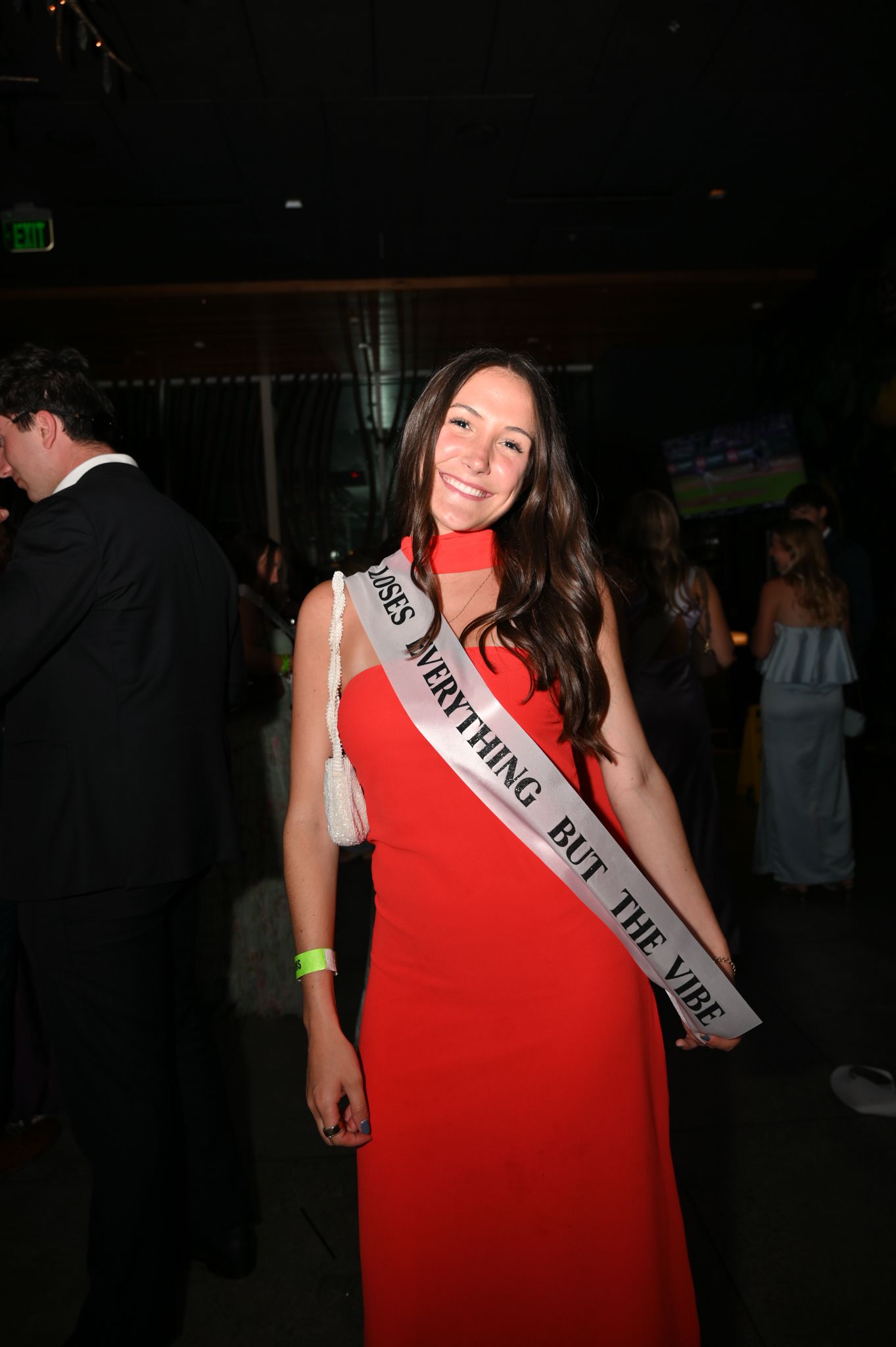 Woman in red gown wearing a pageant sash reading 'Everything But The Vibe' smiling at a formal event.