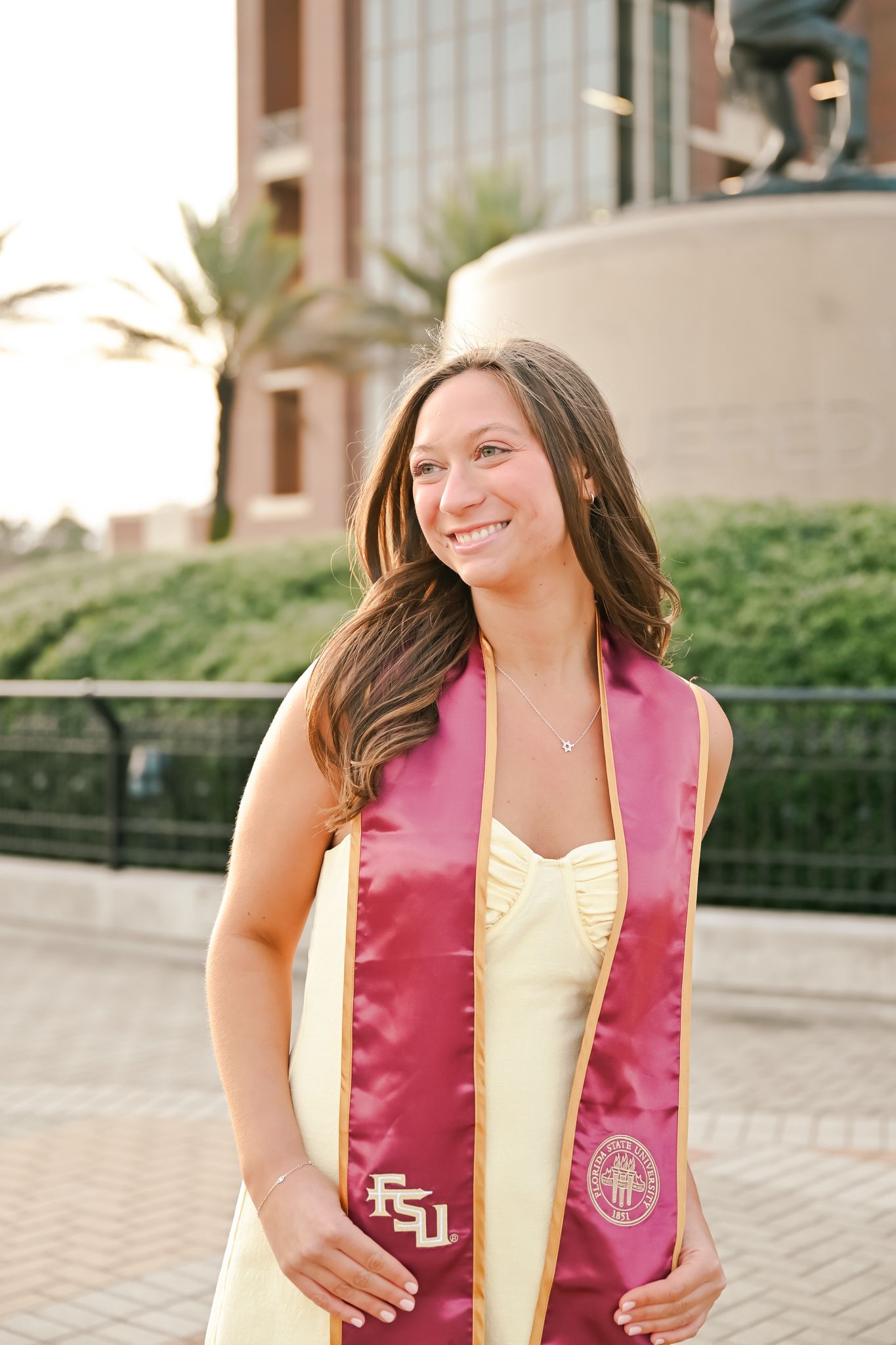 Graduate in a pink and yellow FSU graduation stole smiling during an outdoor photo session.