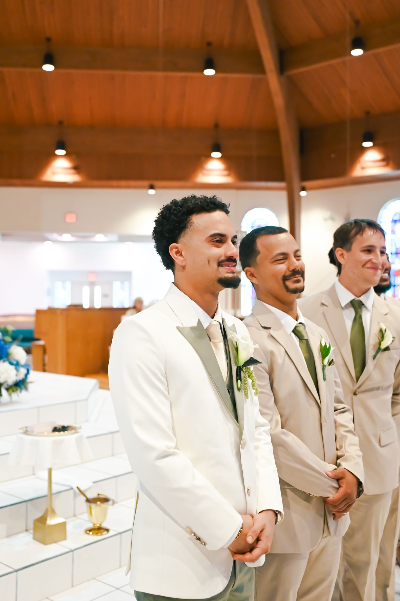 Groomsmen in light beige suits and white shirts stand together laughing during a wedding celebration.
