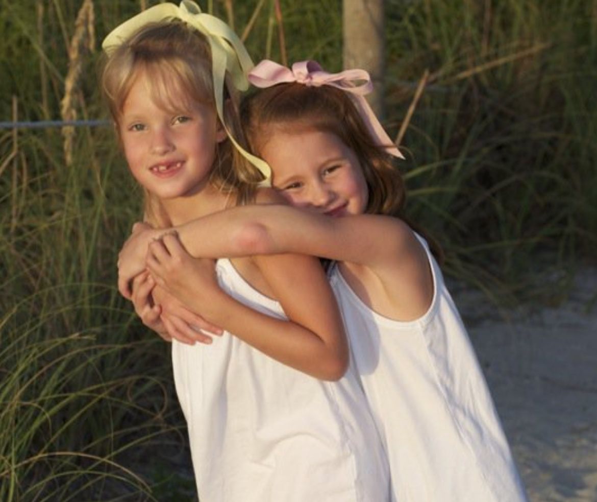 Children in white outfits playing and hugging on beach at sunset. The founder Bella with her sister Ava, together the sister duo behind SP.