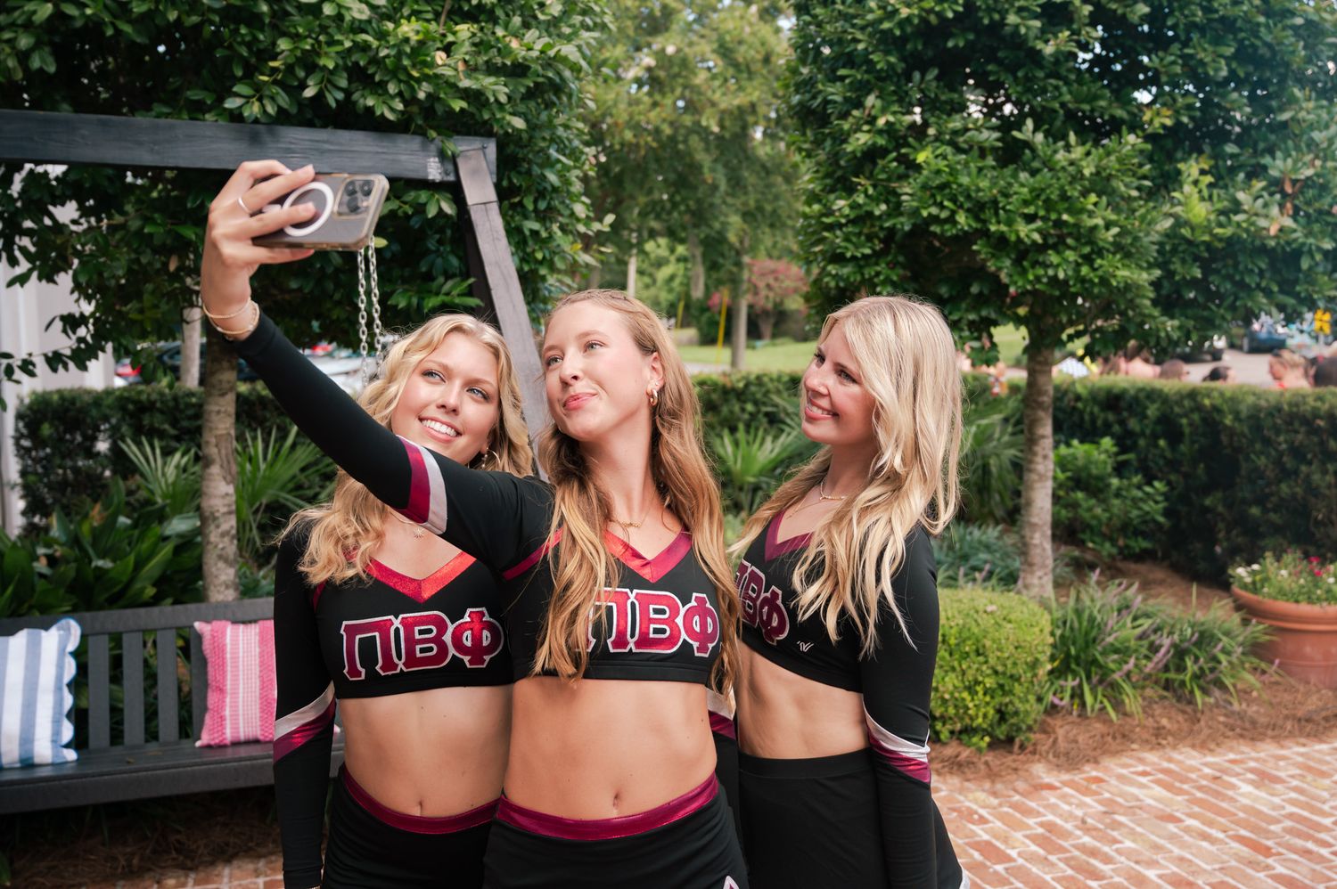 Three blonde sorority girls in Pi Beta Phi uniforms taking a selfie outdoors on a brick patio.