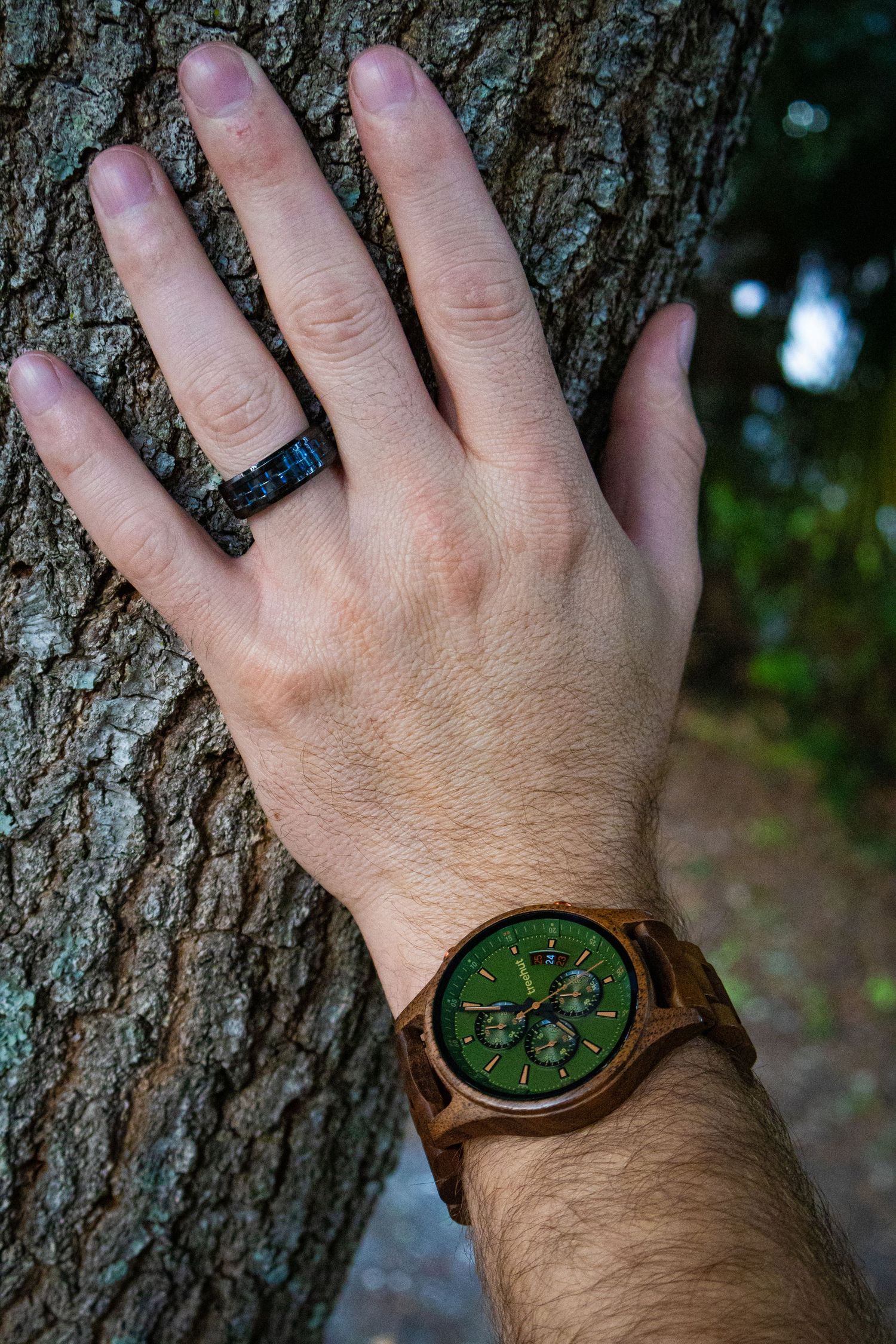 Hand wearing wooden watch pressed against tree bark texture.