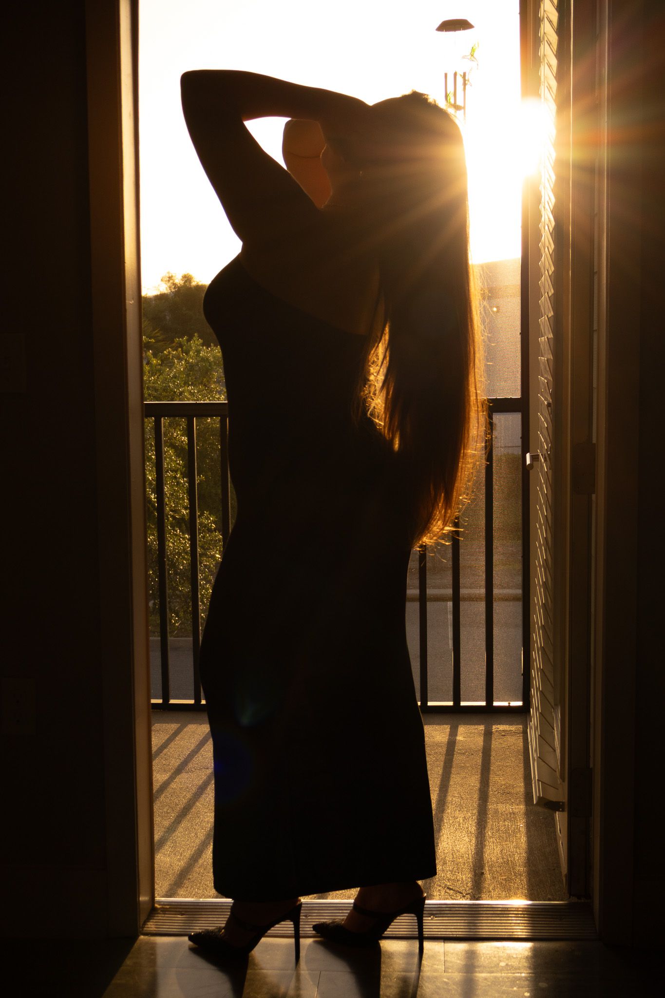 A silhouetted figure stretches against a balcony railing during golden hour sunset creating a dramatic backlit scene.