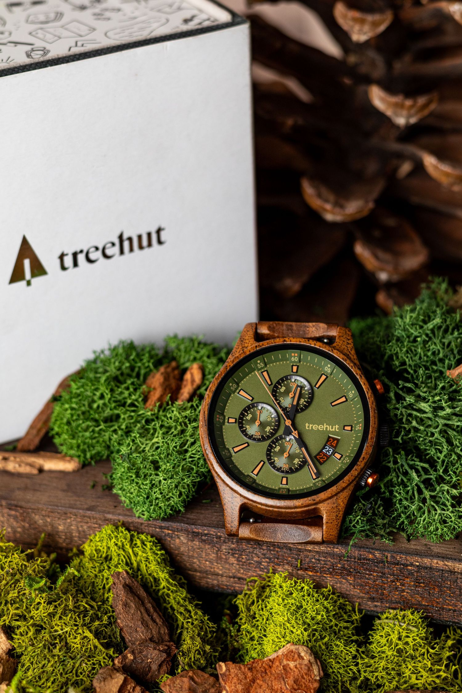 Wooden watch with olive green dial displayed on moss and wood in nature setting.