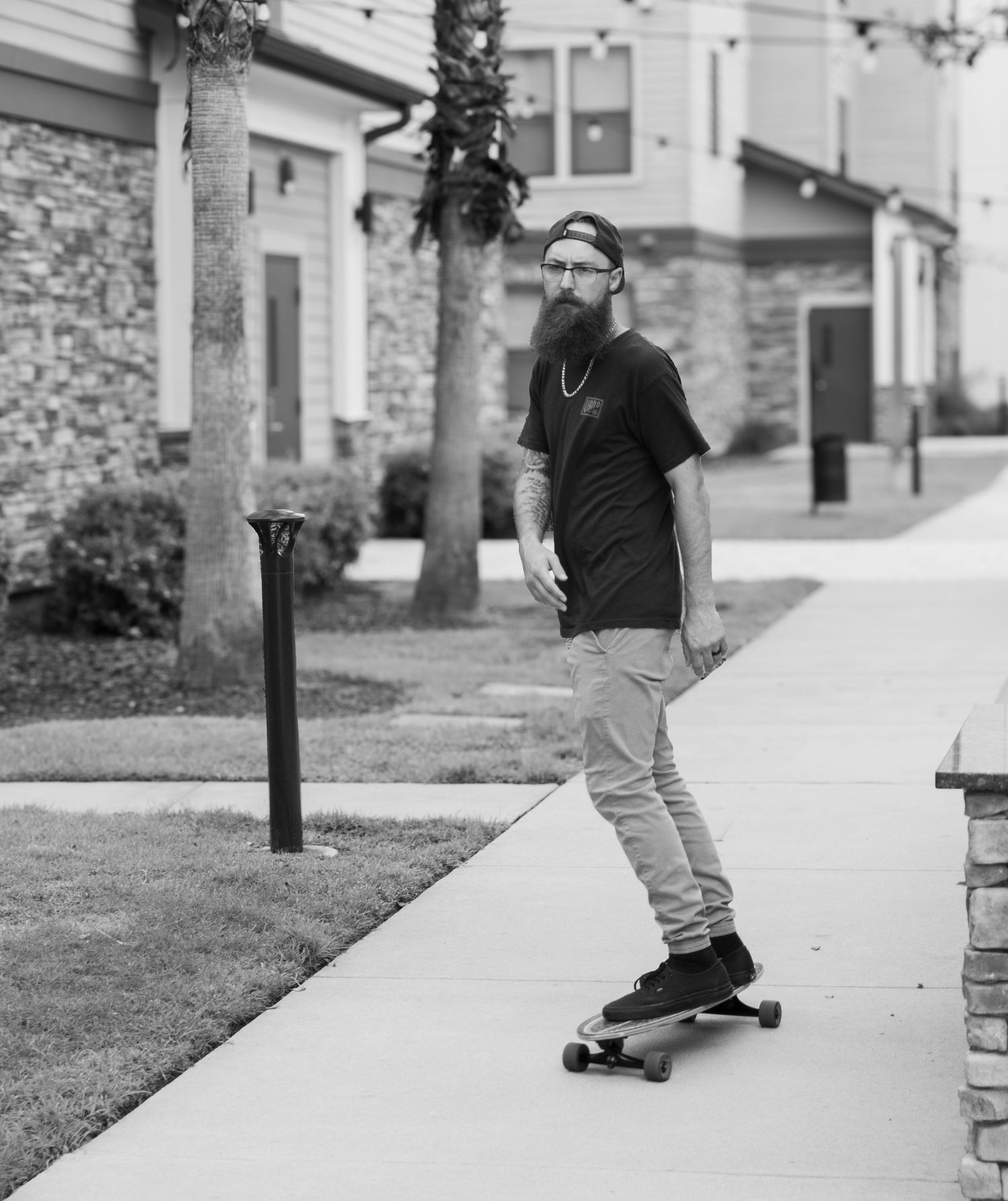 A skateboarder performs a sequence of tricks while riding along a concrete sidewalk in black and white photography.