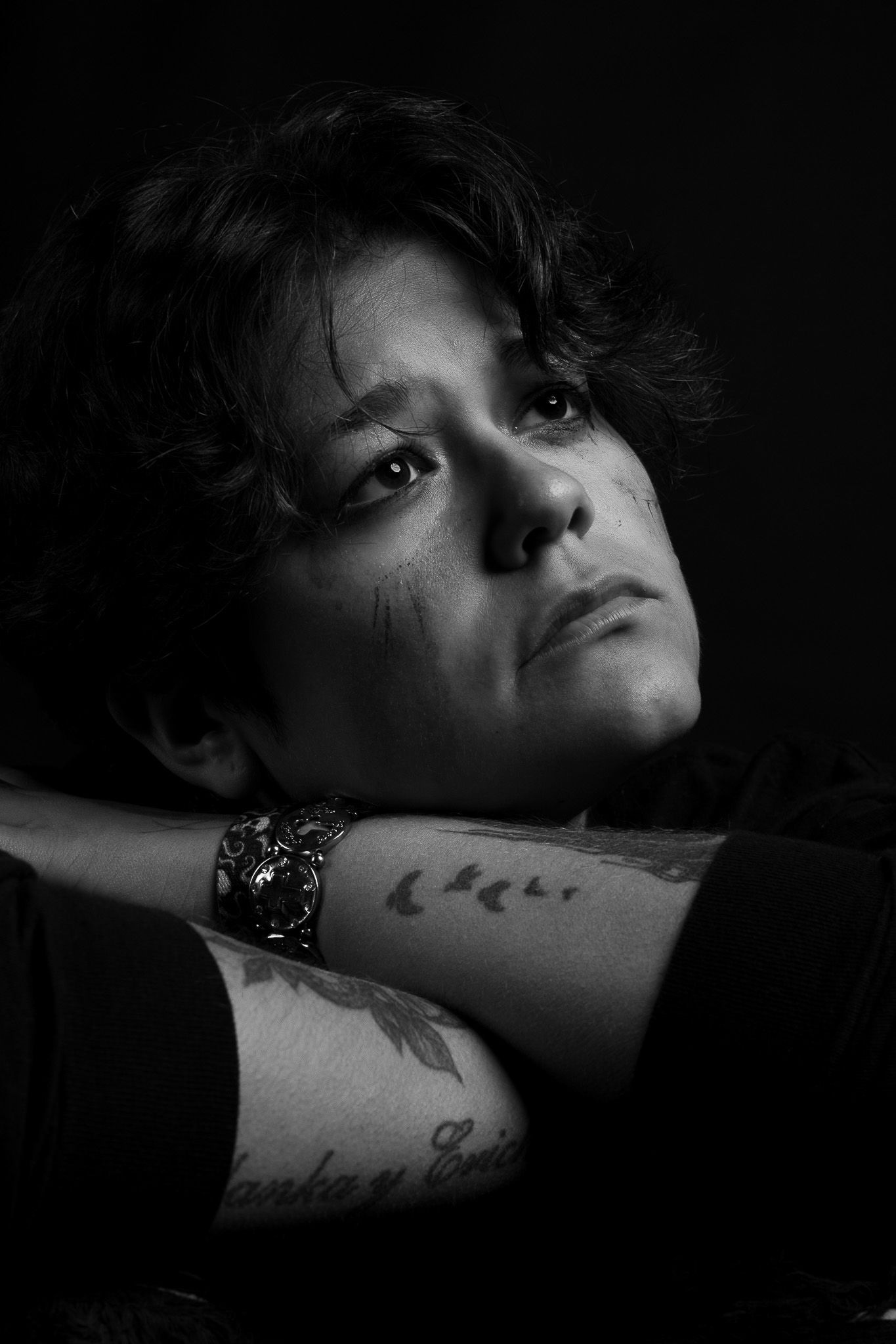 A dramatic black and white photo series showing close-up shots of an arm with tattoos against a dark background.