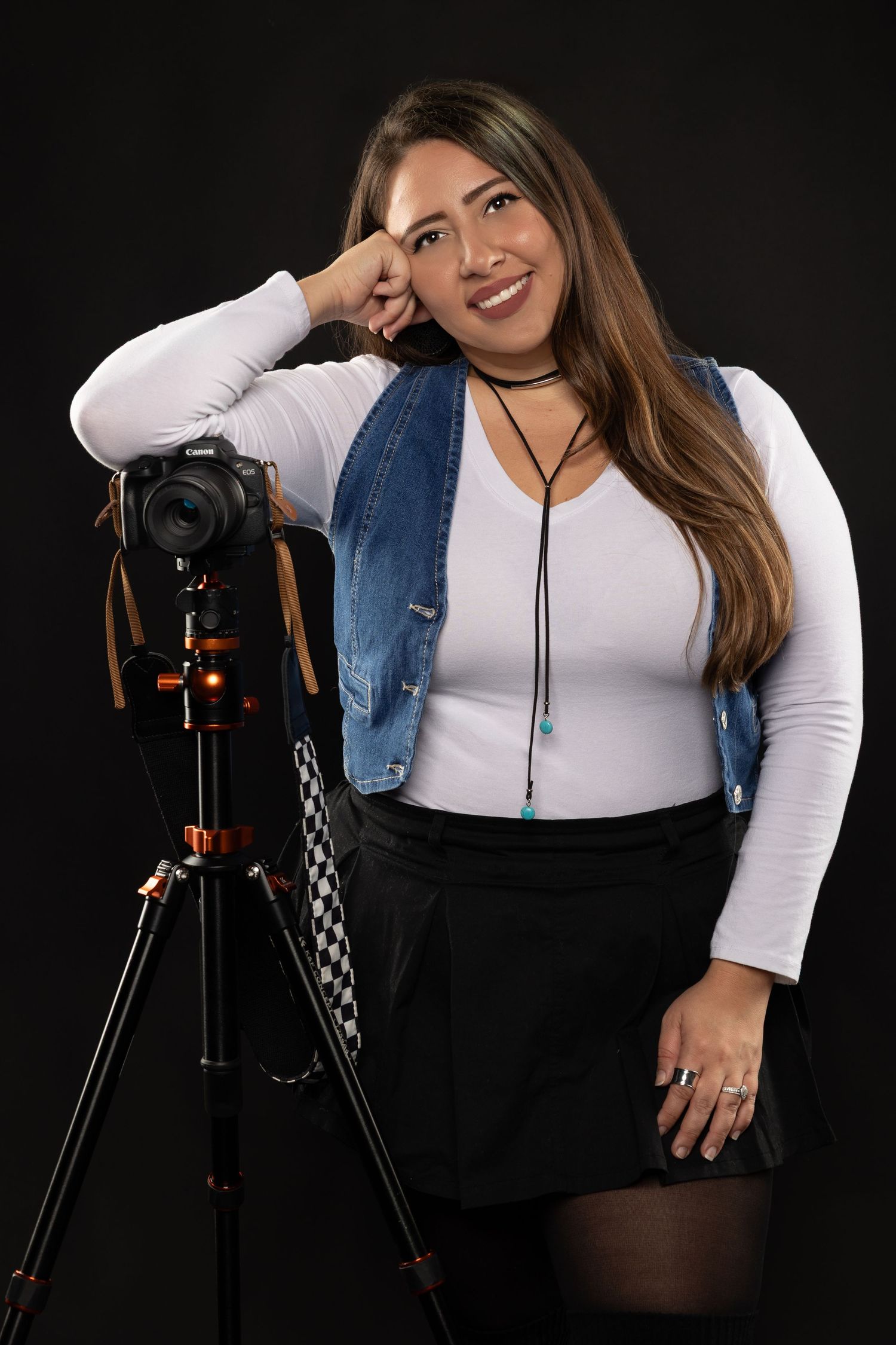 Photographer demonstrates posing techniques with a camera on tripod against dark background in studio setting.