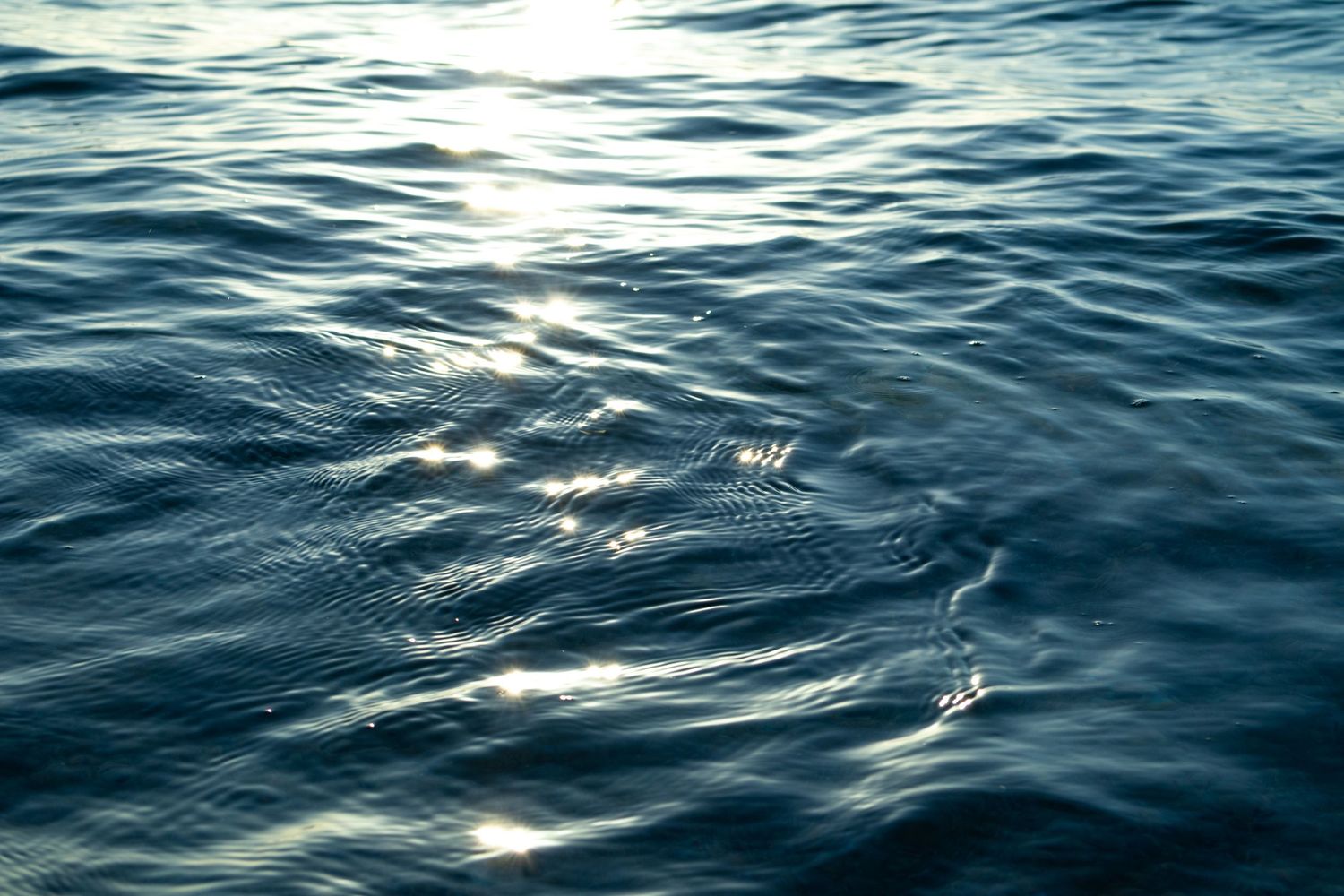 Sunlight sparkles on dark blue ocean waves creating a mesmerizing pattern of rippling water and reflections.