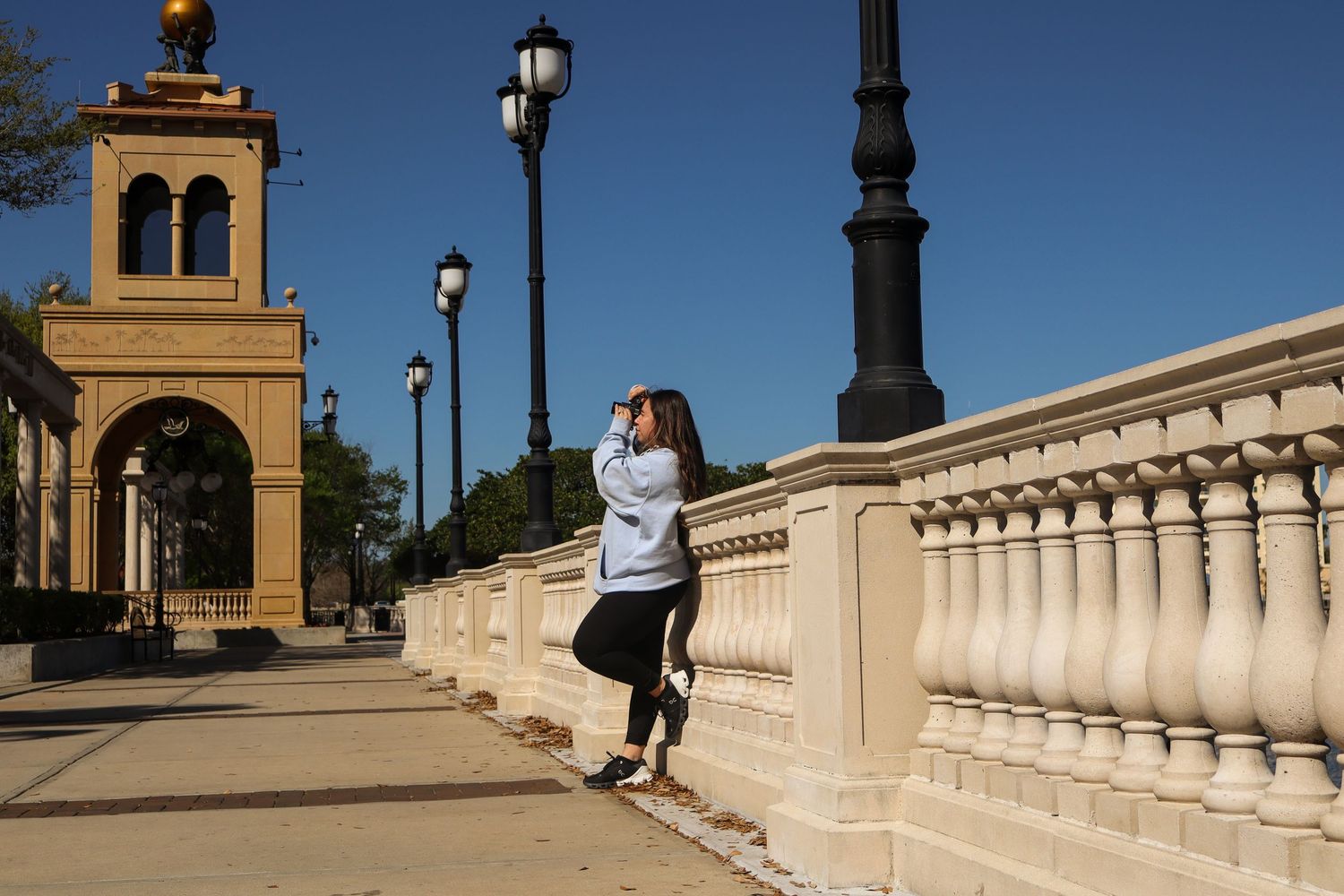 A person in white athletic wear leans against stone balustrade near historic architecture.