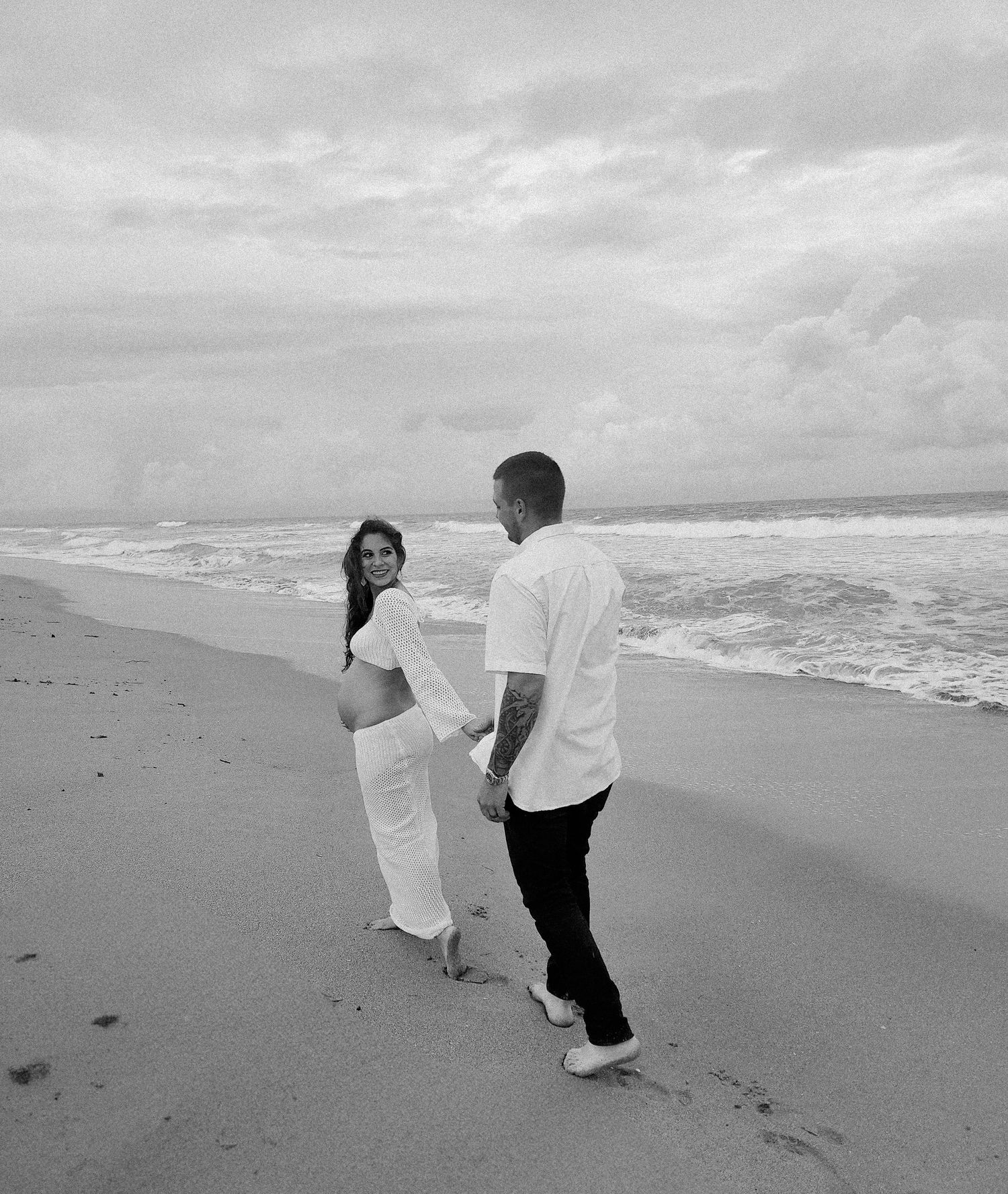 A couple walks along a misty beach shore in black and white.