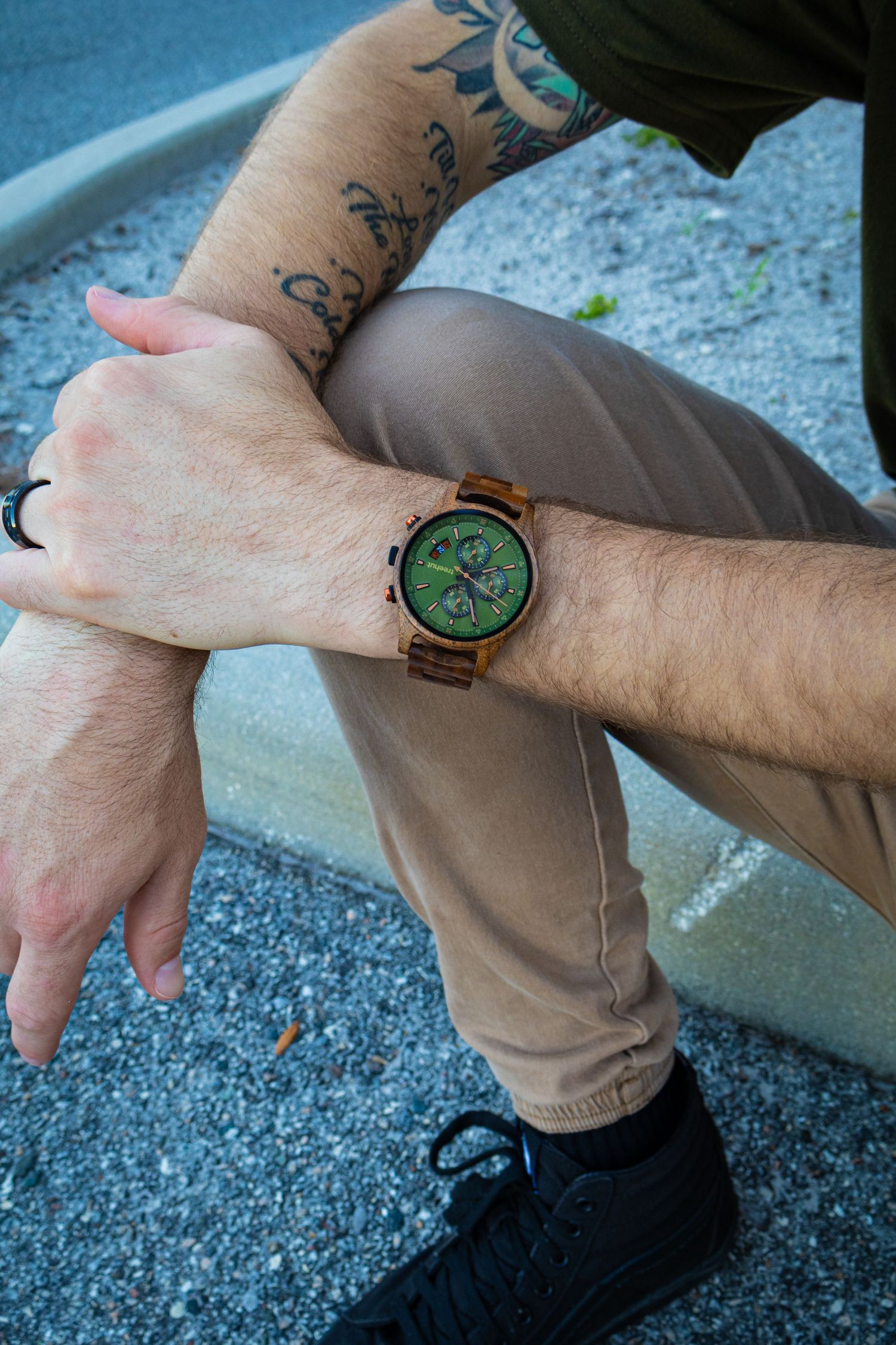 Wooden chronograph watch with green face displayed on person's wrist outdoors.