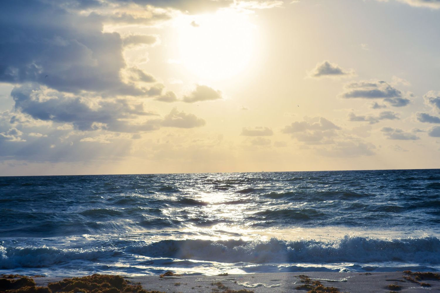 Dramatic ocean seascape with sunbeams breaking through clouds over rolling waves at sunset.