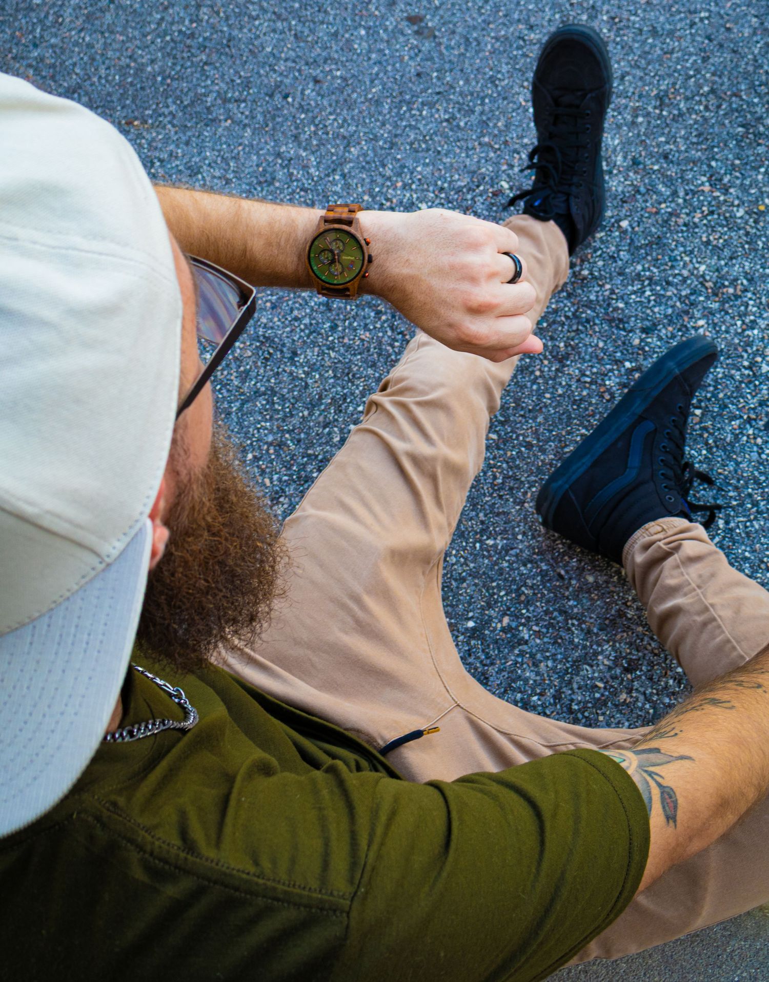 Wooden watch with green dial worn on wrist against asphalt background.