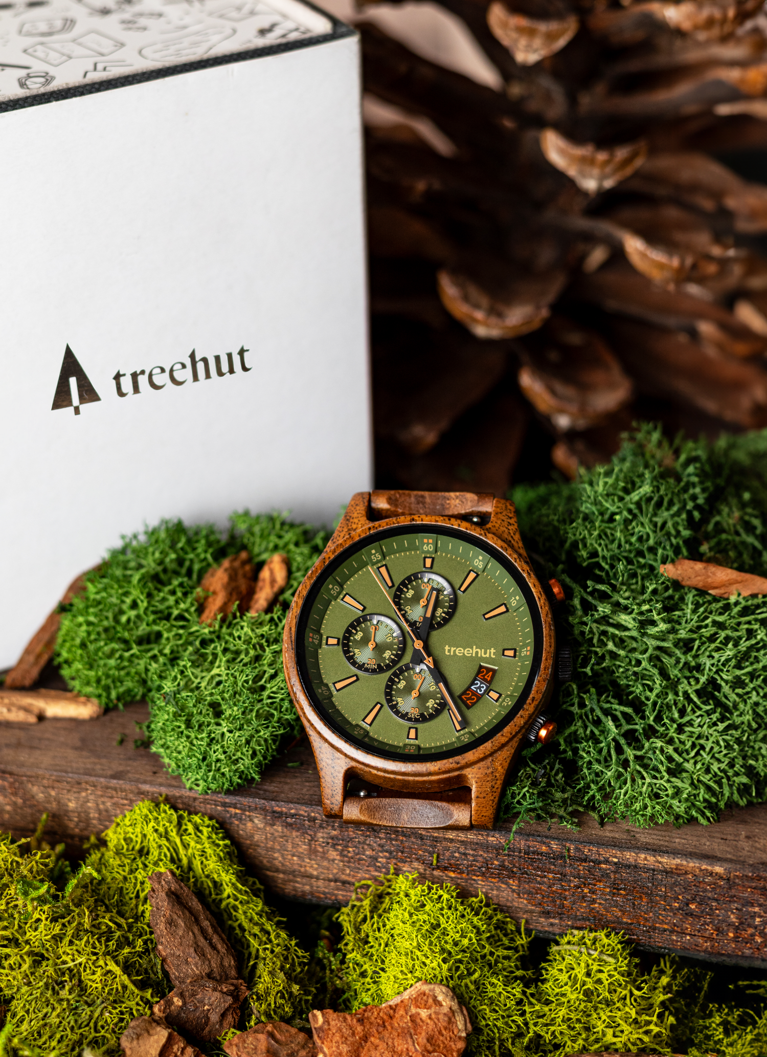 A wooden watch with green chronograph dial and wooden strap displayed on moss-covered wood in natural lighting. Product shot