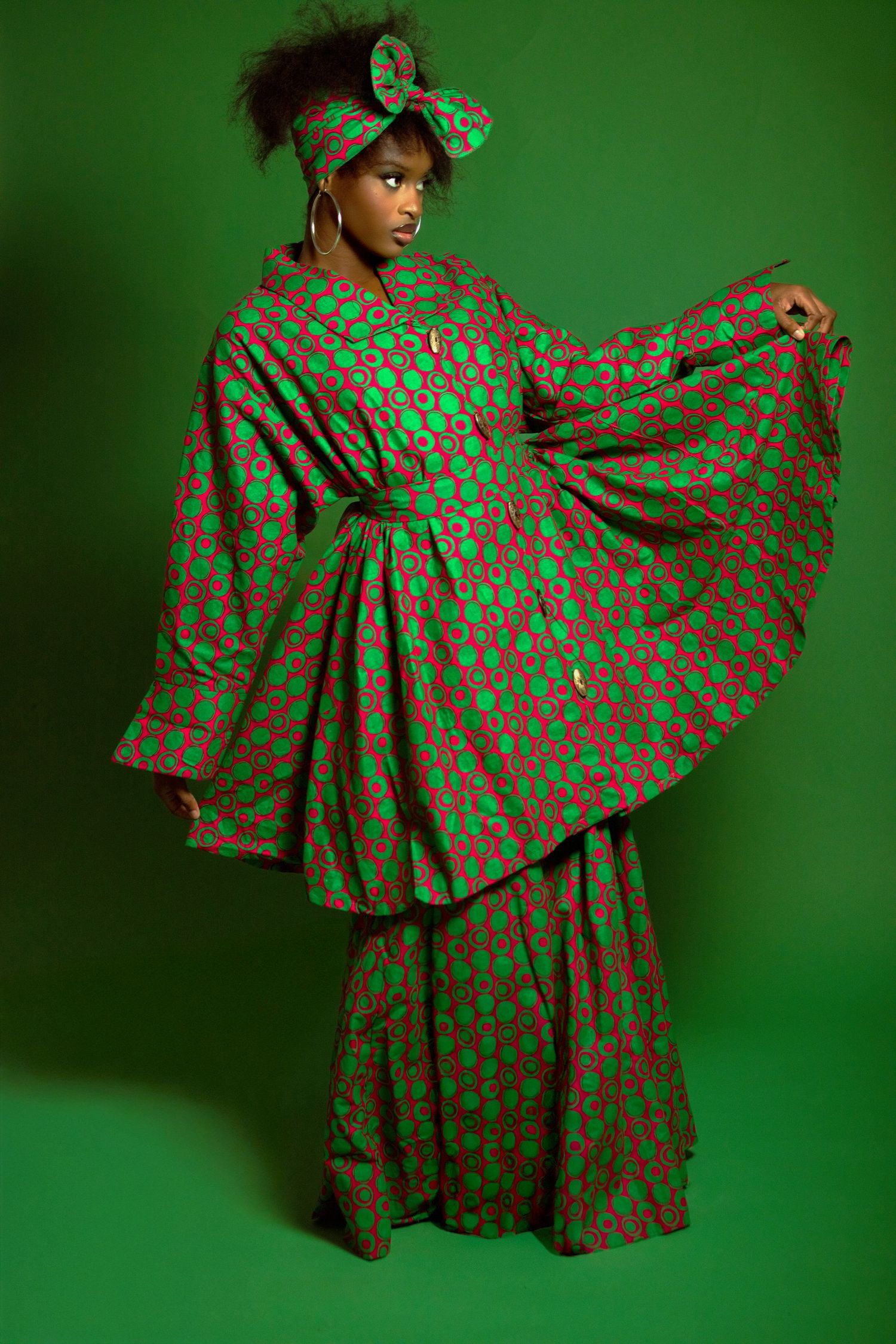 Model showcasing vibrant green African print ensemble with wide sleeves and matching headwrap on green background.