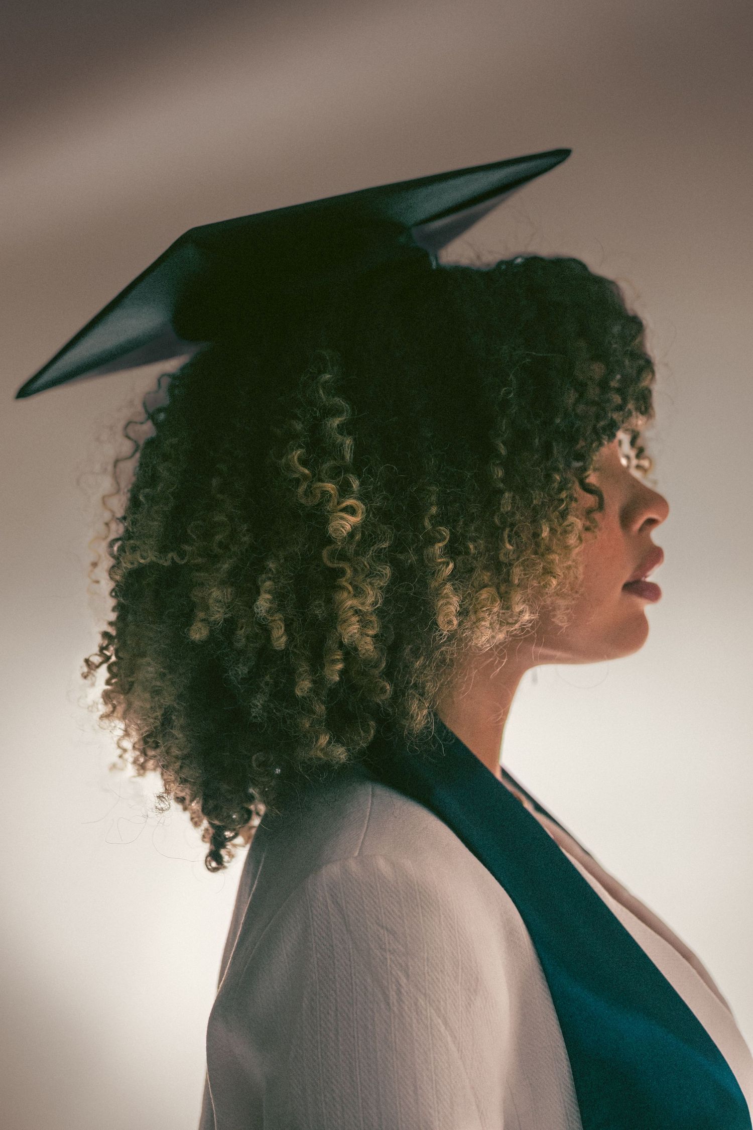 Side profile of a young woman with curly hair wearing a graduation cap.