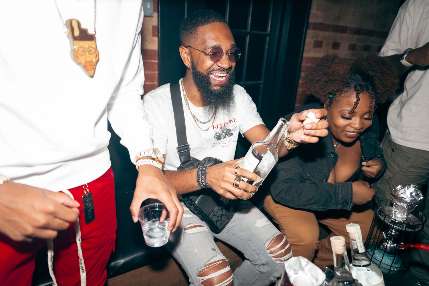 Smiling bearded man in white shirt enjoys drinks with friends at a lively nightclub party.