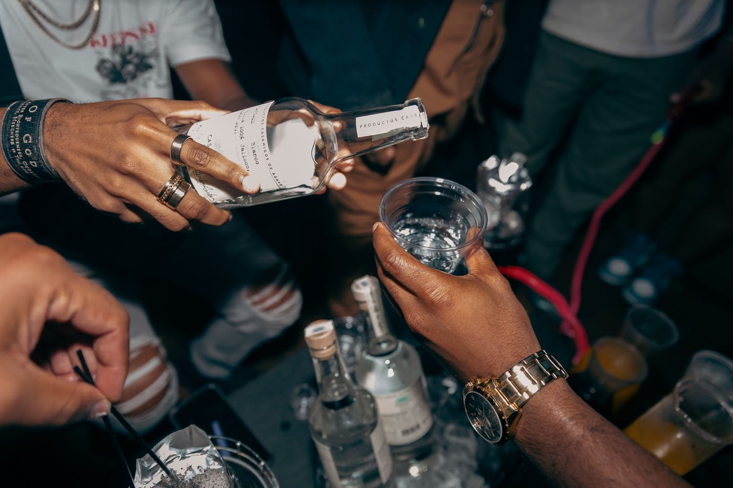 Hands pouring clear spirits into glasses at a nightclub party celebration event.