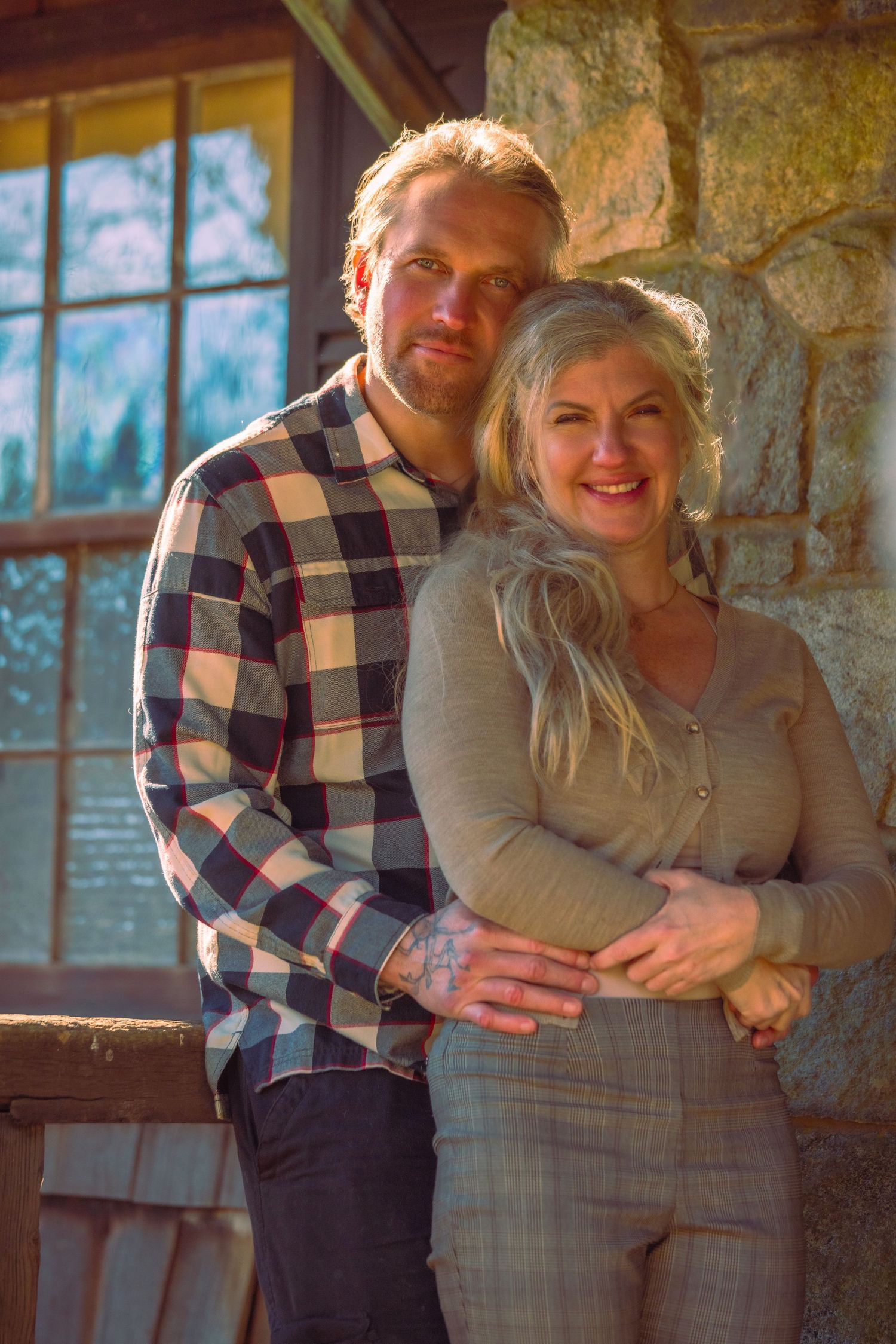 Smiling couple embracing warmly in golden light outside a rustic stone building.