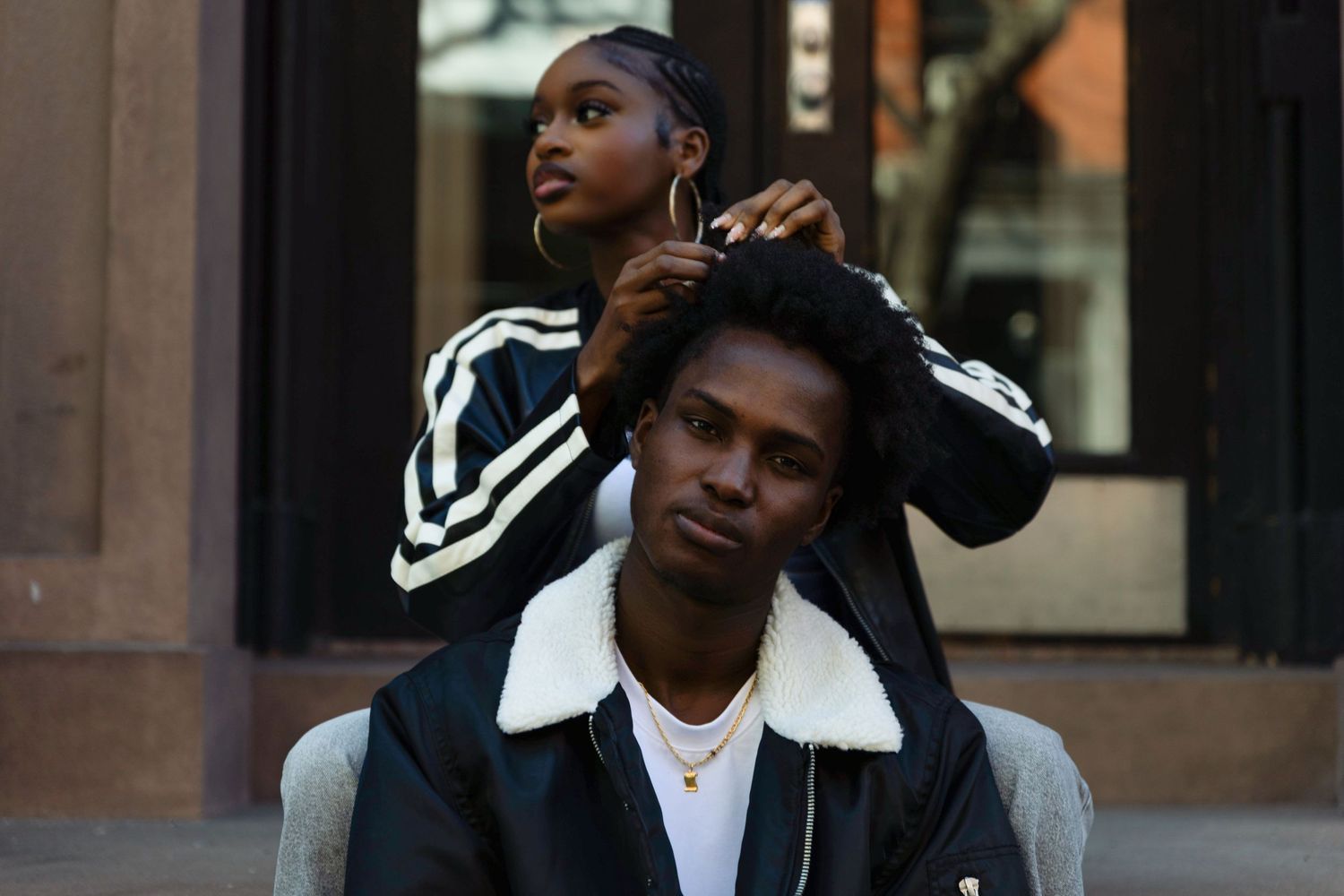 Young woman styling a man's hair outdoors on a city street.