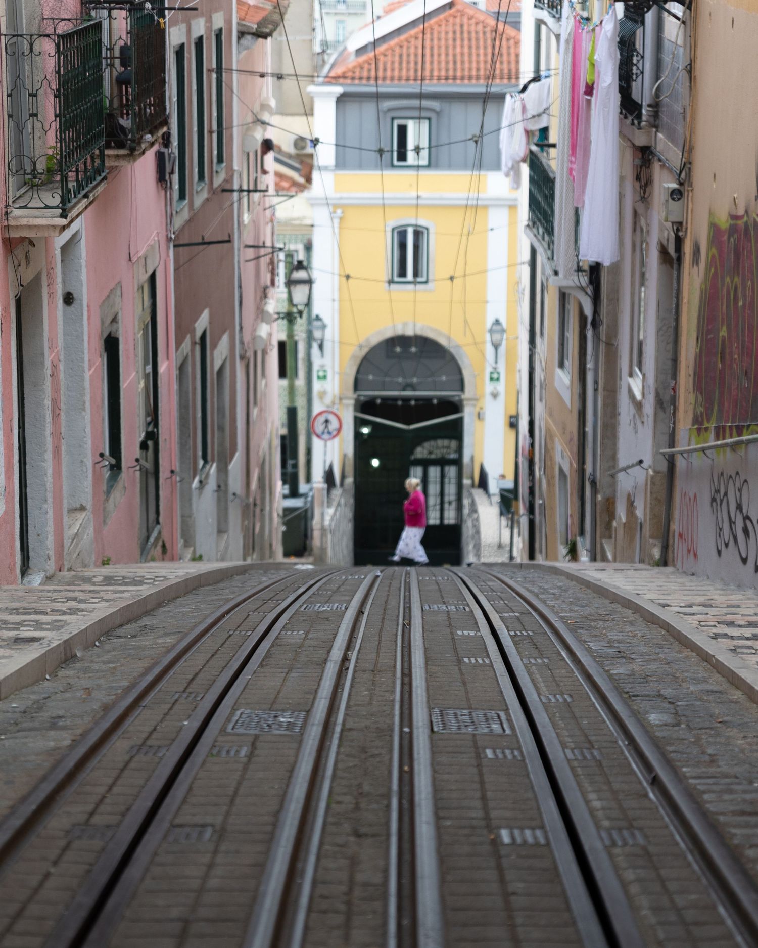 Steep cobblestone street with tram tracks leading downhill between colorful buildings in Lisbon, Portugal.