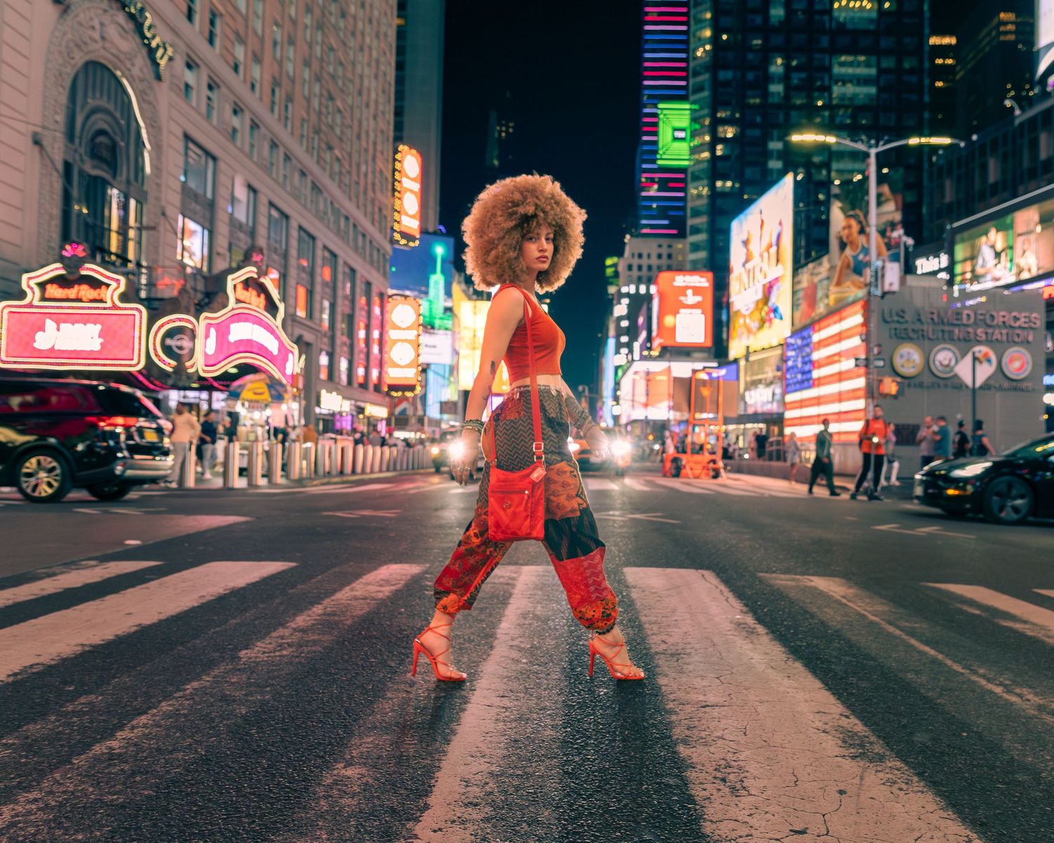 Woman in vibrant red outfit crossing a busy Times Square street at night.