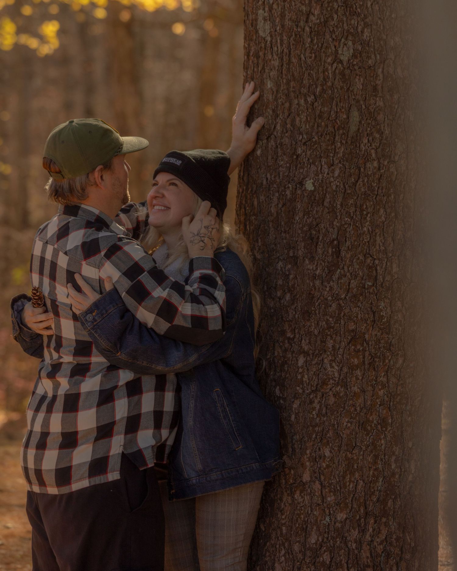Young couple sharing a romantic moment leaning against a tree in autumn forest setting.
