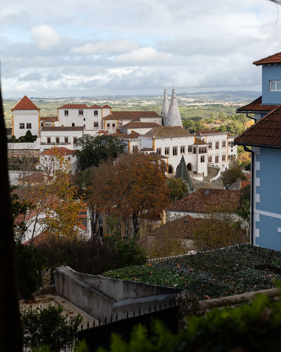 Aerial view of Sintra National Palace with twin chimneys surrounded by autumn trees and landscape.