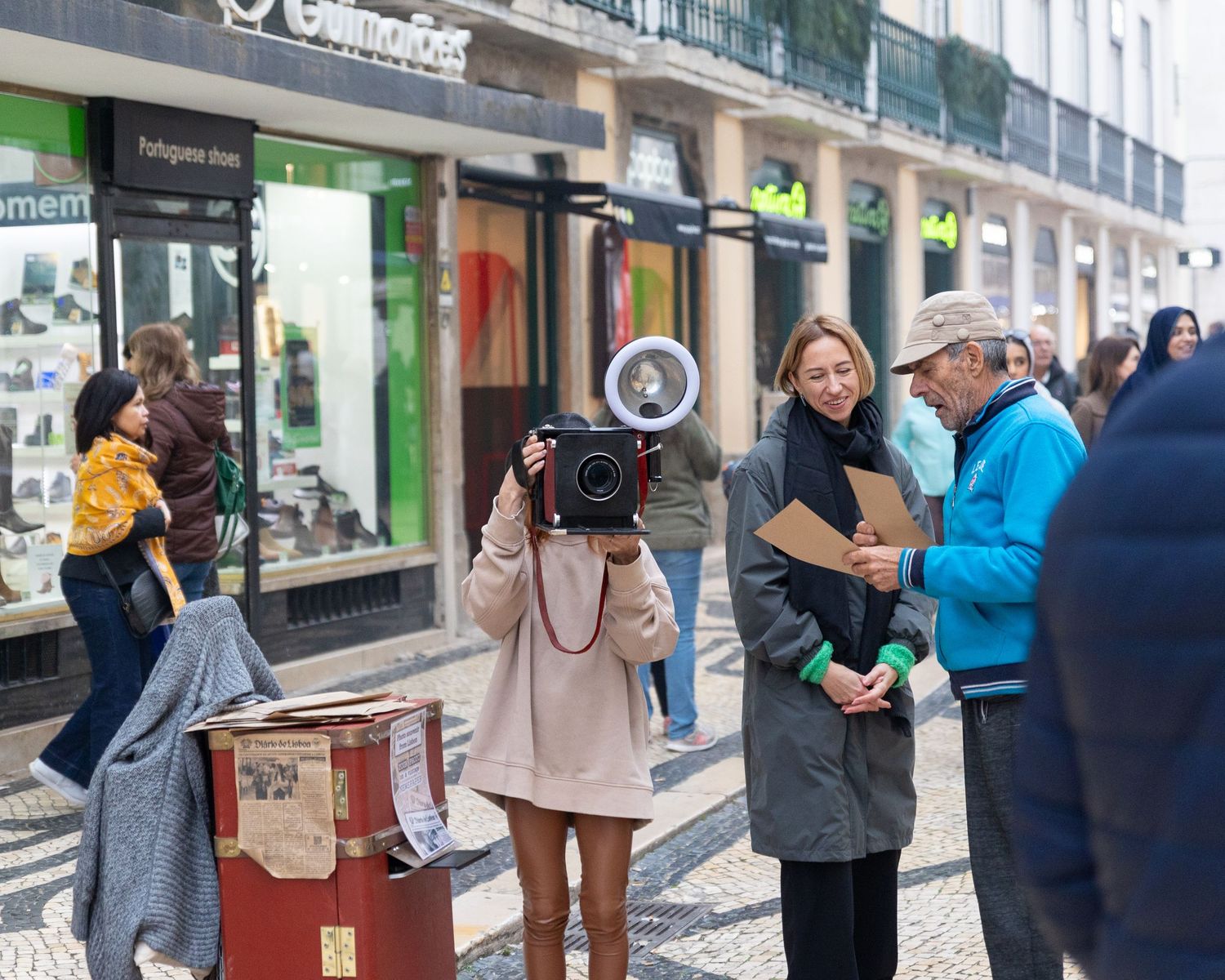 Woman using vintage camera on a busy pedestrian shopping street with smiling bystanders nearby.