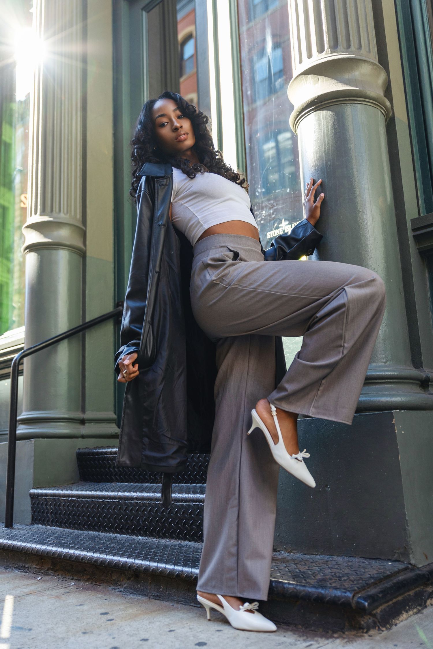 Fashionable woman in wide-leg pants and leather coat posing on city steps.