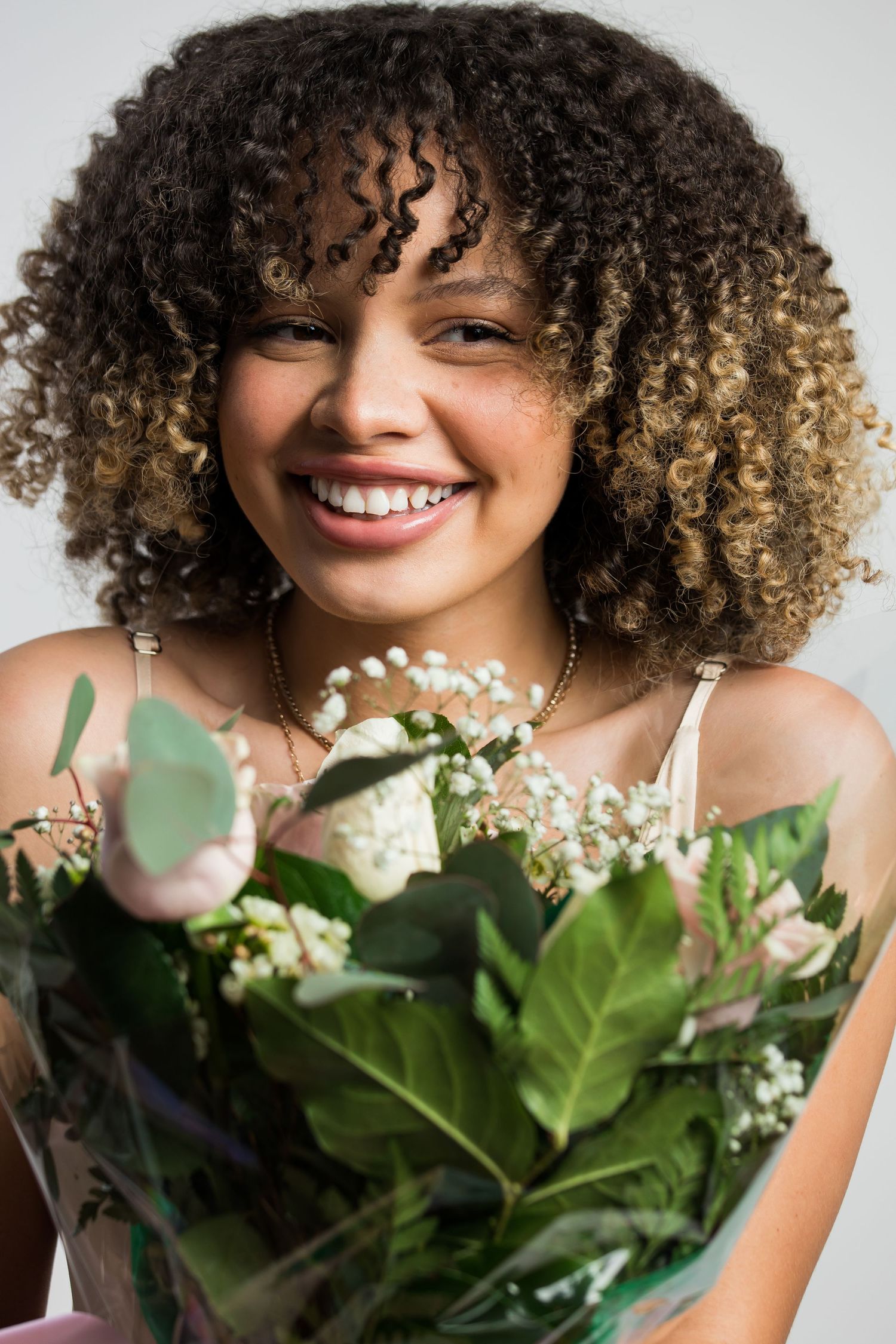 Smiling young woman with curly hair holding a bouquet of fresh flowers.