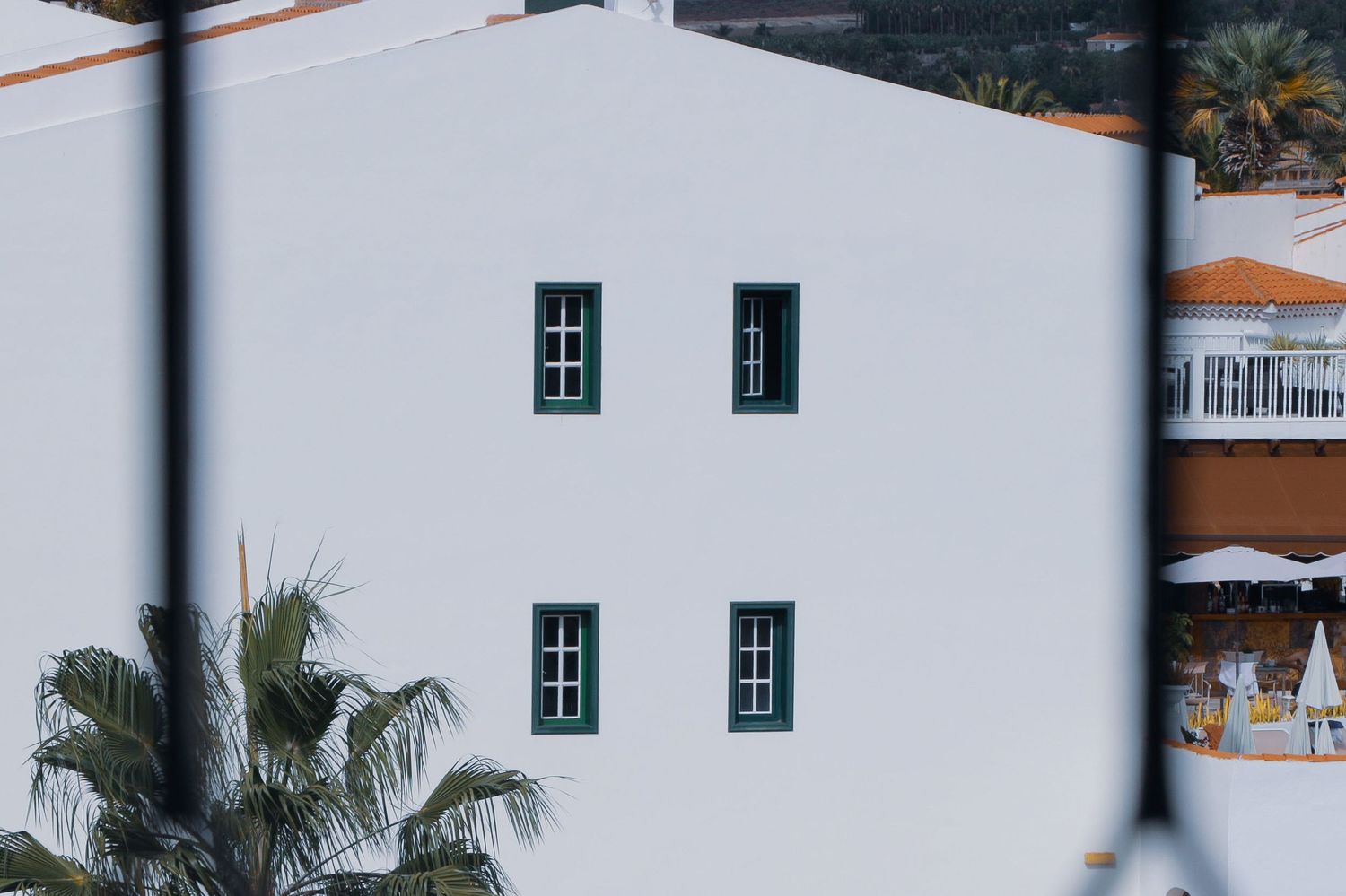 White Mediterranean-style building with green-framed windows and palm trees in the foreground.