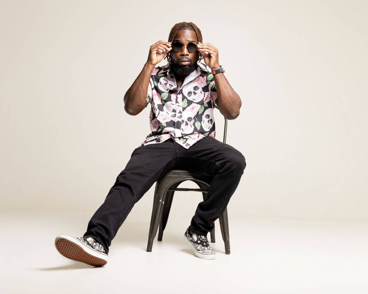 Man in floral shirt and sunglasses posing on chair in studio.