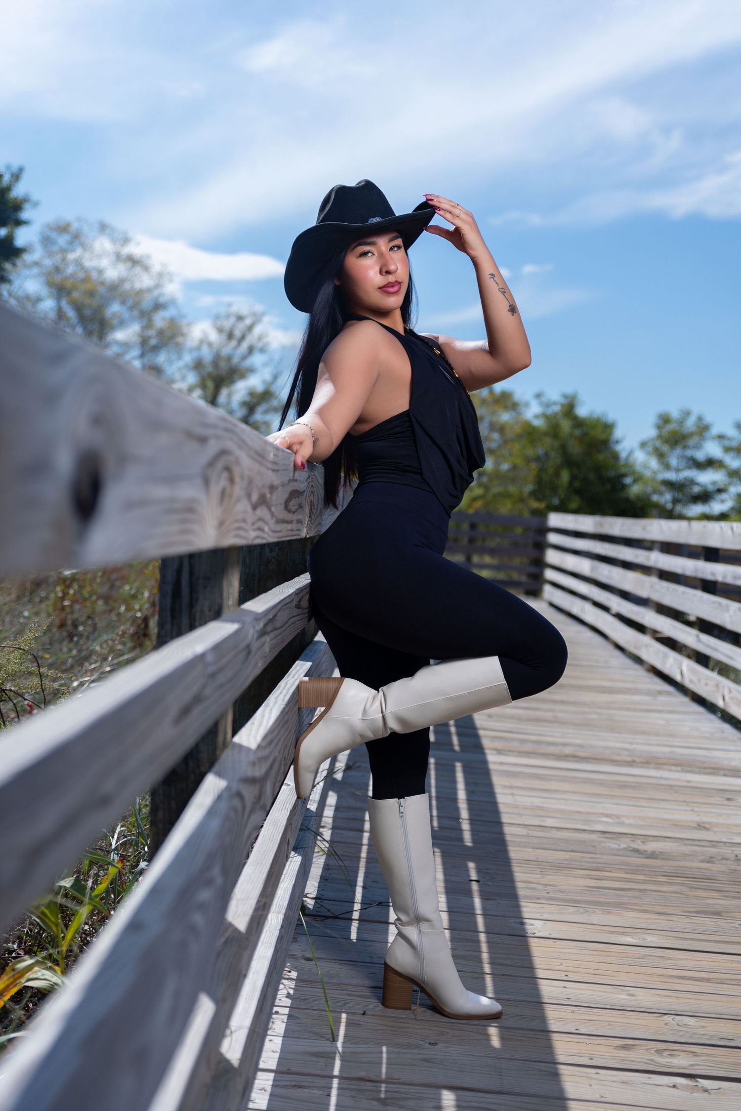 Asian woman in black bodysuit and white cowboy boots posing on wooden boardwalk.