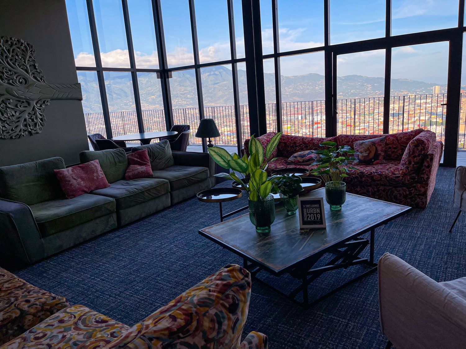 Modern high-rise lounge with floor-to-ceiling windows overlooking a mountain cityscape with stylish sofas.