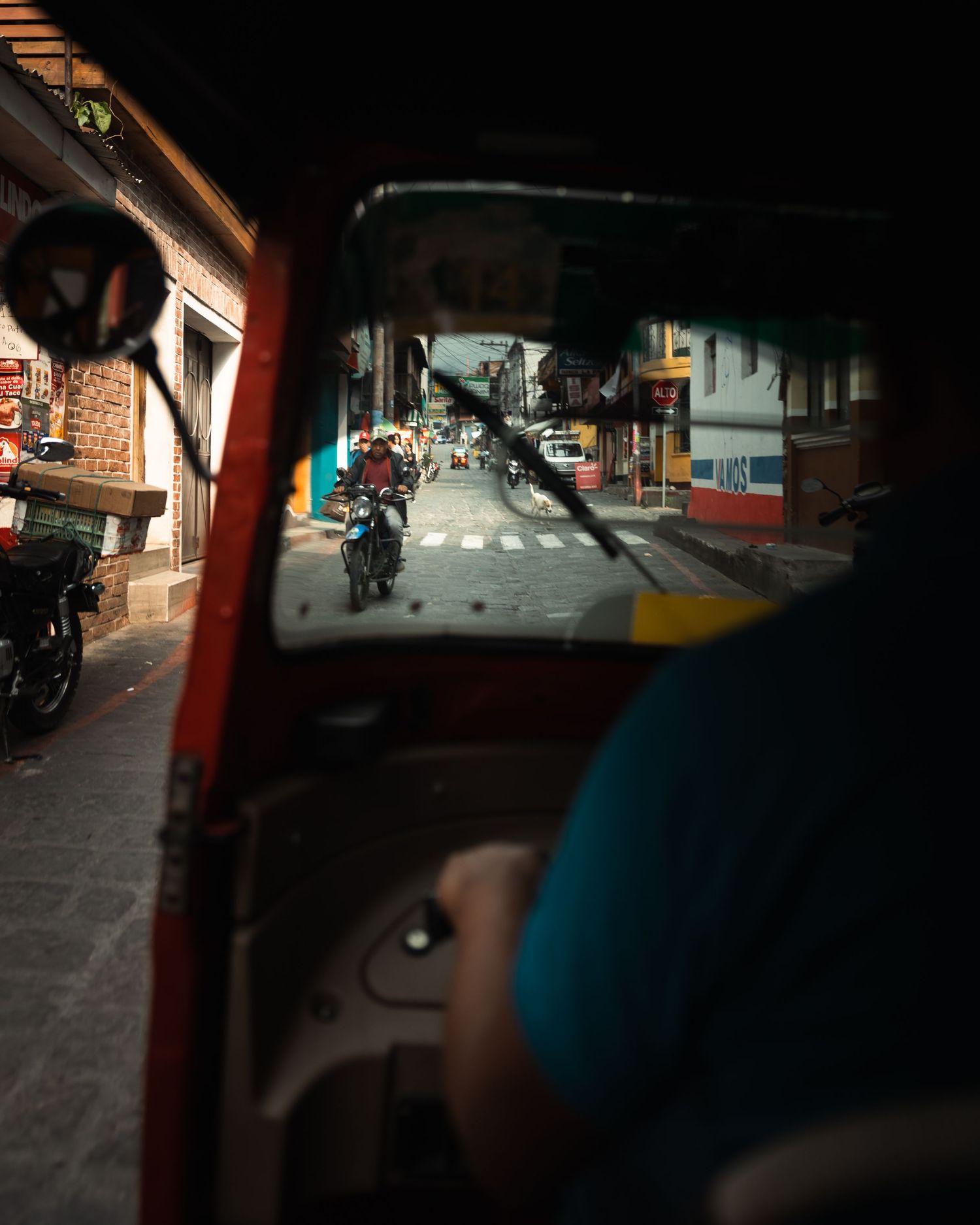 View from inside a tuk-tuk of a narrow urban street with motorcycles.