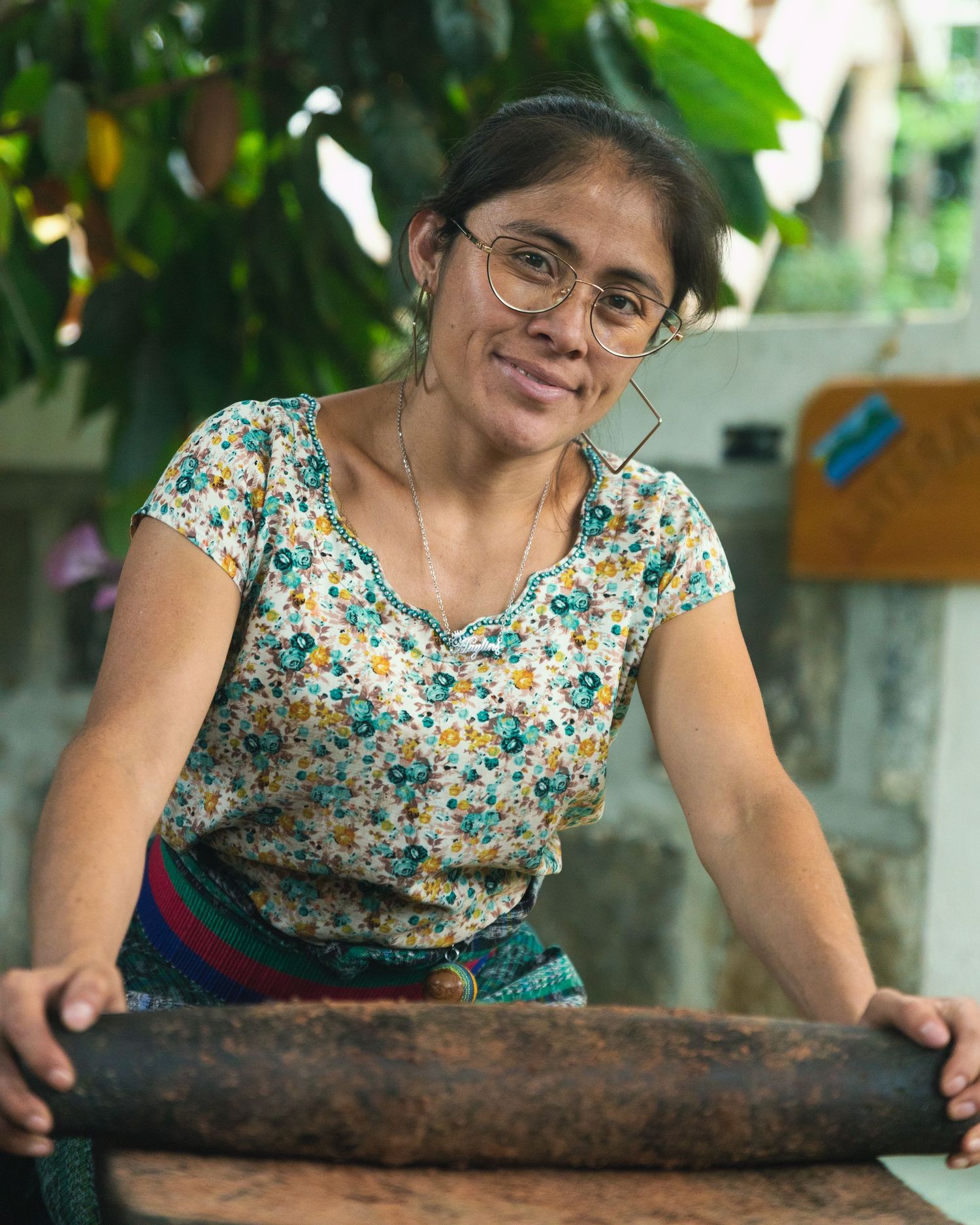 Smiling woman with glasses leaning on a rustic wooden roller outdoors.