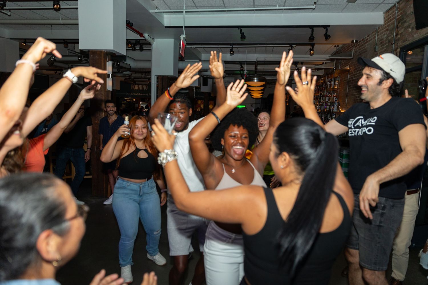 Diverse group of people dancing and celebrating with raised hands at lively indoor social event.